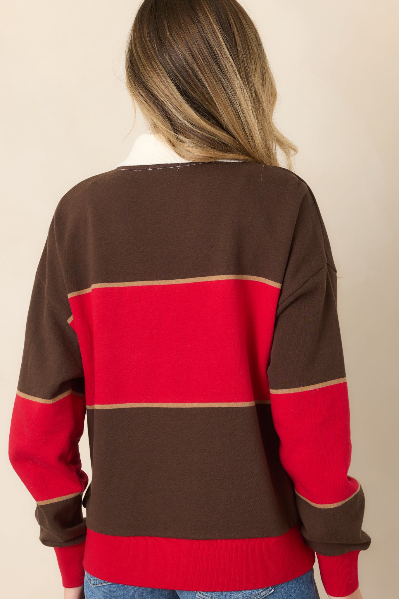 Rear view of the red and chocolate brown colorblock sweatshirt showing its relaxed fit, dropped shoulders, long sleeves, and ribbed hem.
