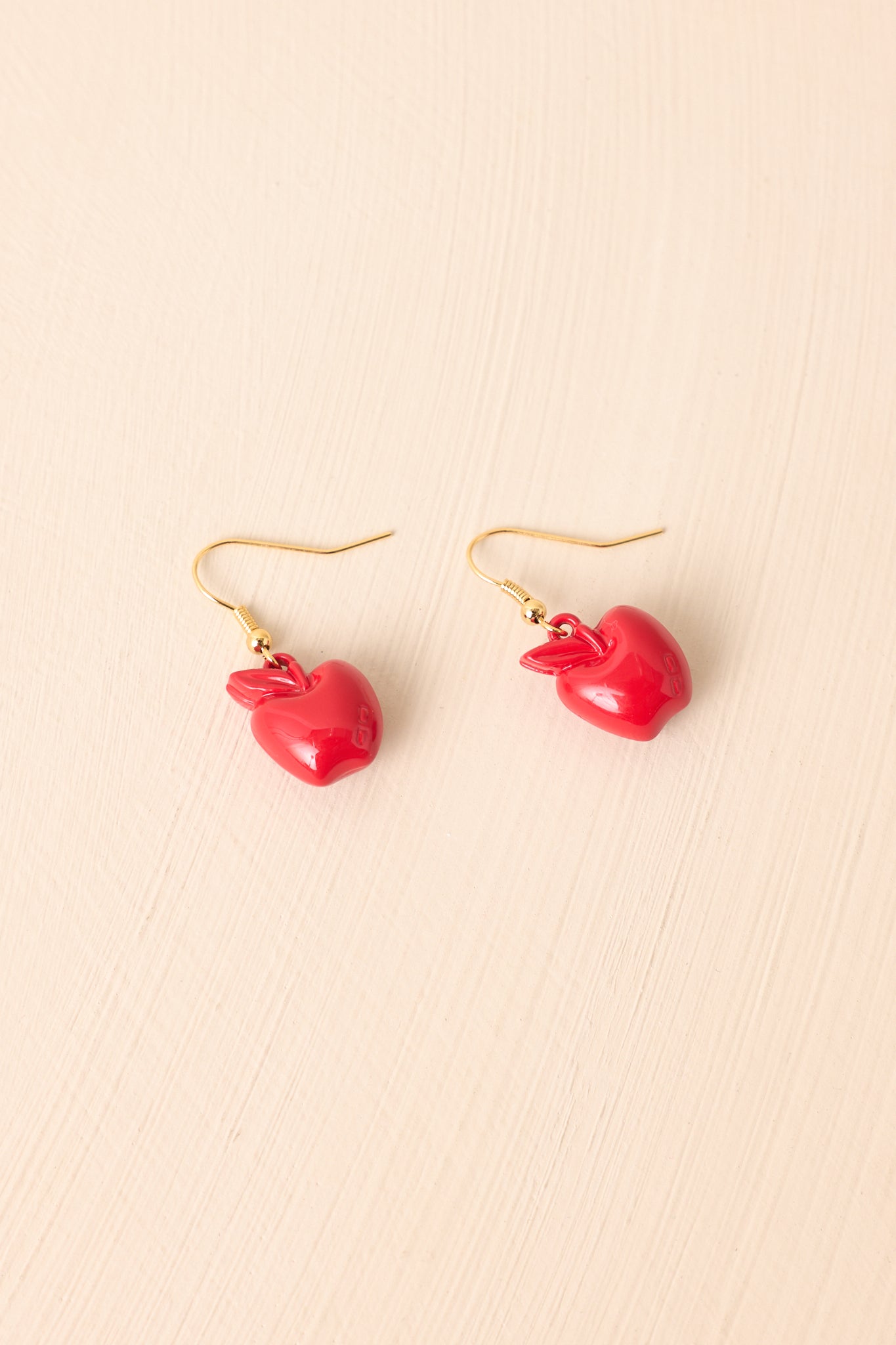 Red drop charm earrings displayed against a beige background, featuring the gold fish hook backs.
