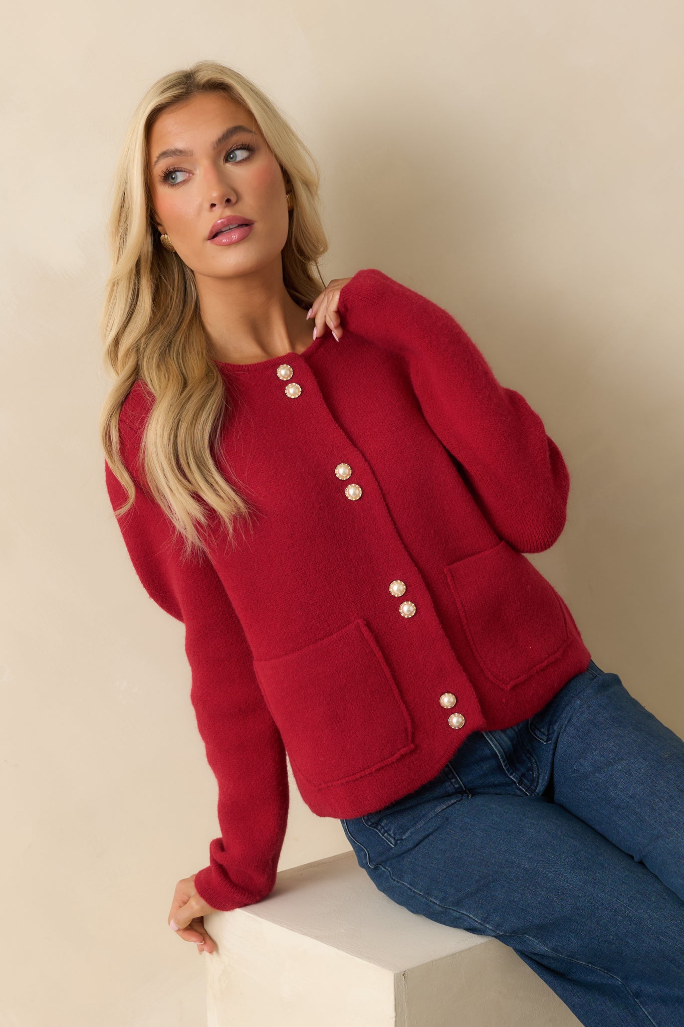 Red knit cardigan with a round neckline, front button closure with pearl-accent buttons, long sleeves, and front patch pockets.