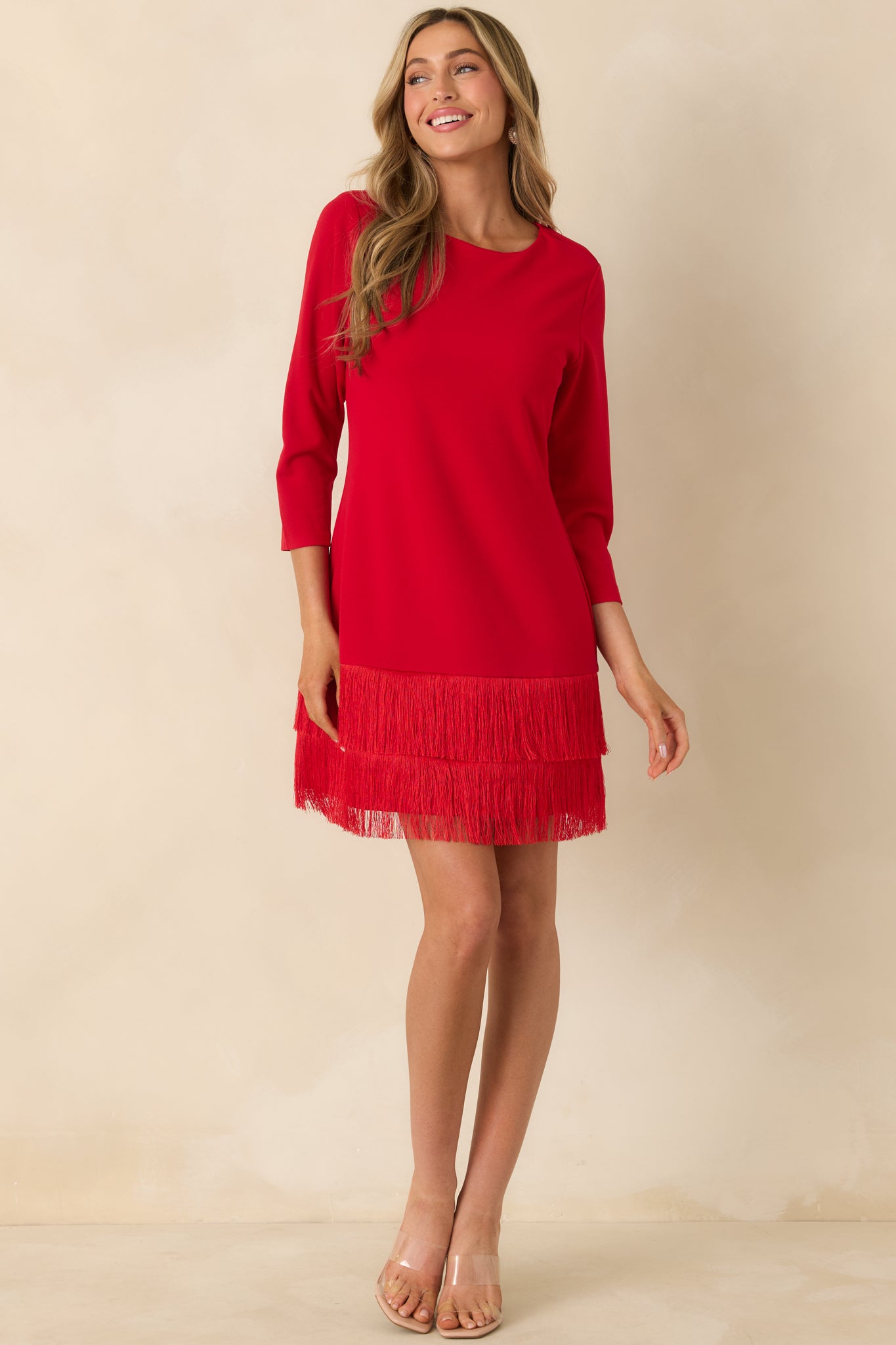 Red mini dress with a round neckline, 3/4-length sleeves, and a tiered fringe hem creating texture and movement.