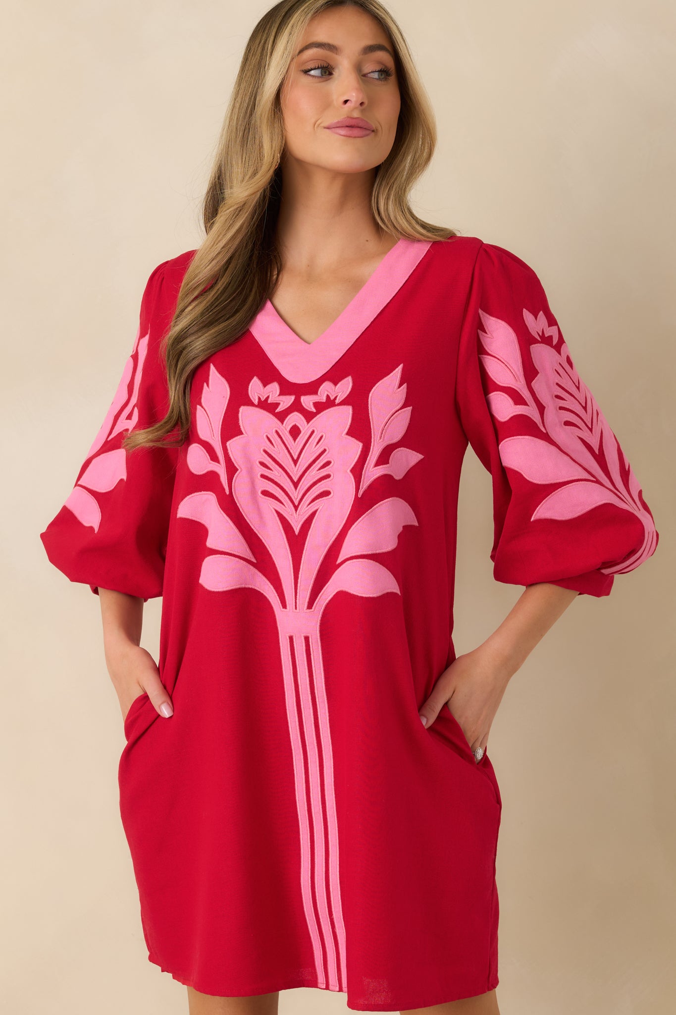 Close view of the red and pink mini dress highlighting the V-neckline, contrast trim, and puff sleeves with gathered cuffs.