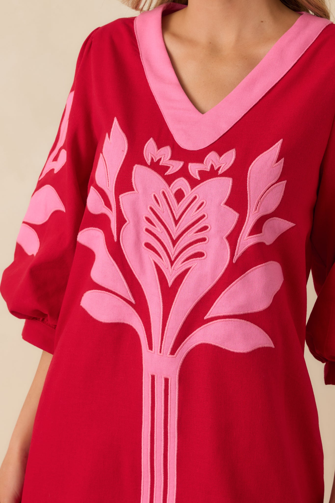 Close-up of the red and pink woven fabric, showing the contrast trim along the V-neckline and gathered cuff details.