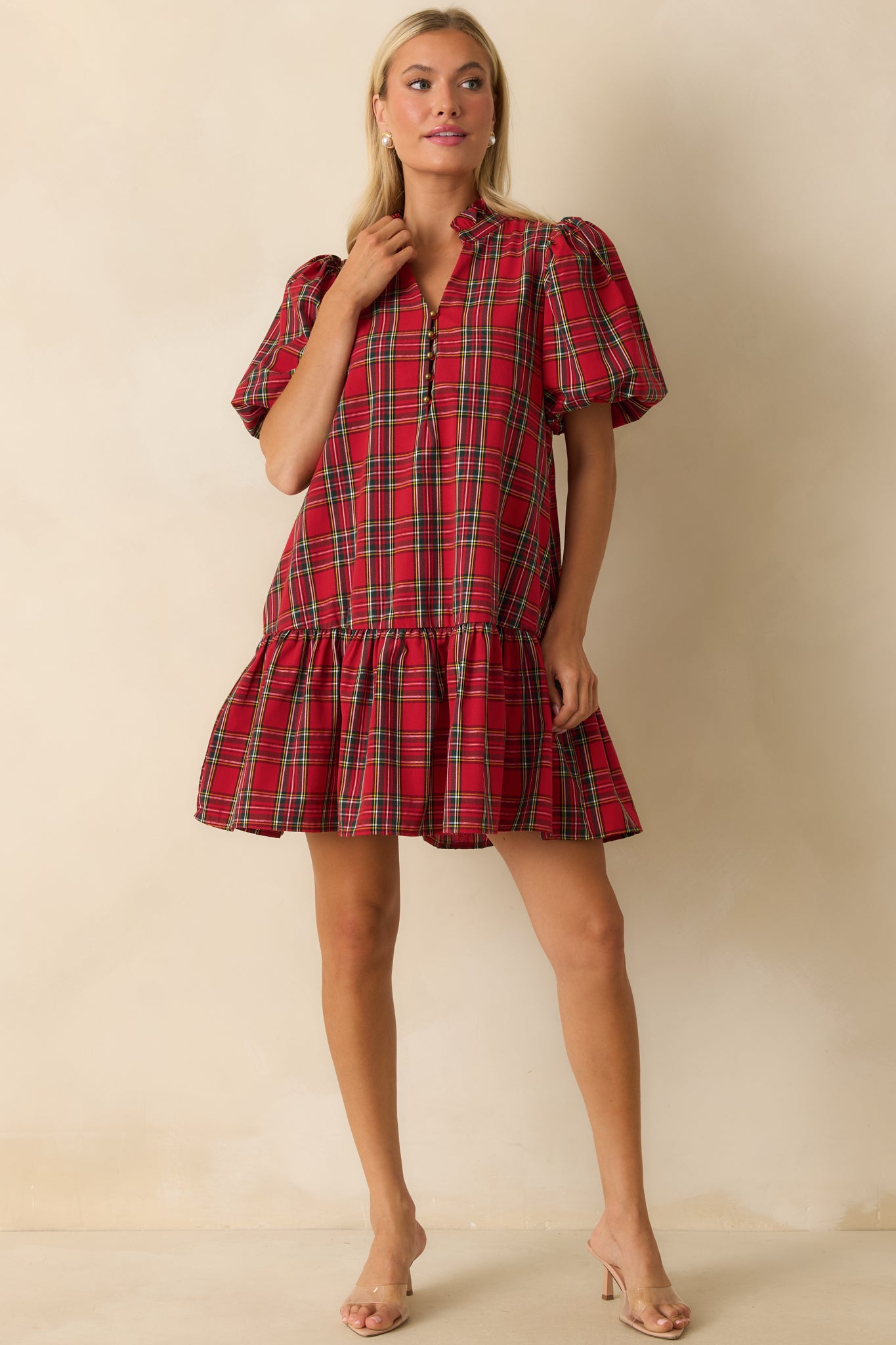Mini dress in red plaid highlighting split neckline with buttons, side pockets, and flowing ruffled drop hem.