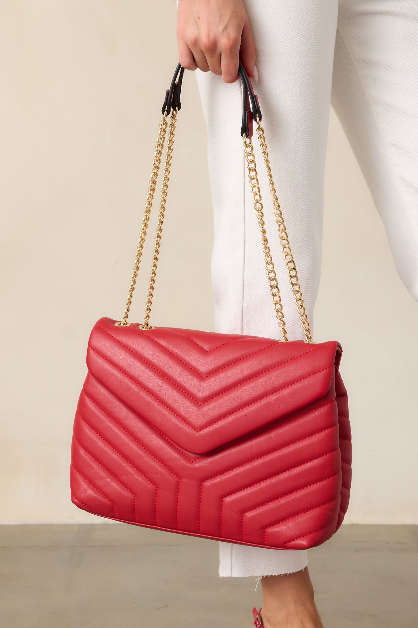 A red quilted rectangular handbag with a snap flap closure and red zipper closure, featuring two gold chain handles with red faux leather handles.