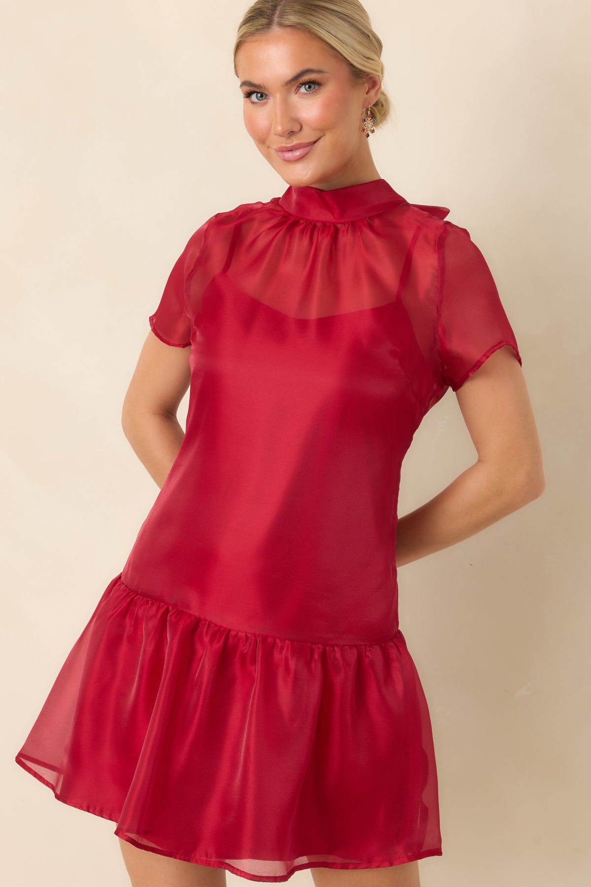 Red mini dress highlighting the sheer mock neckline and translucent short sleeves above the lined bodice.