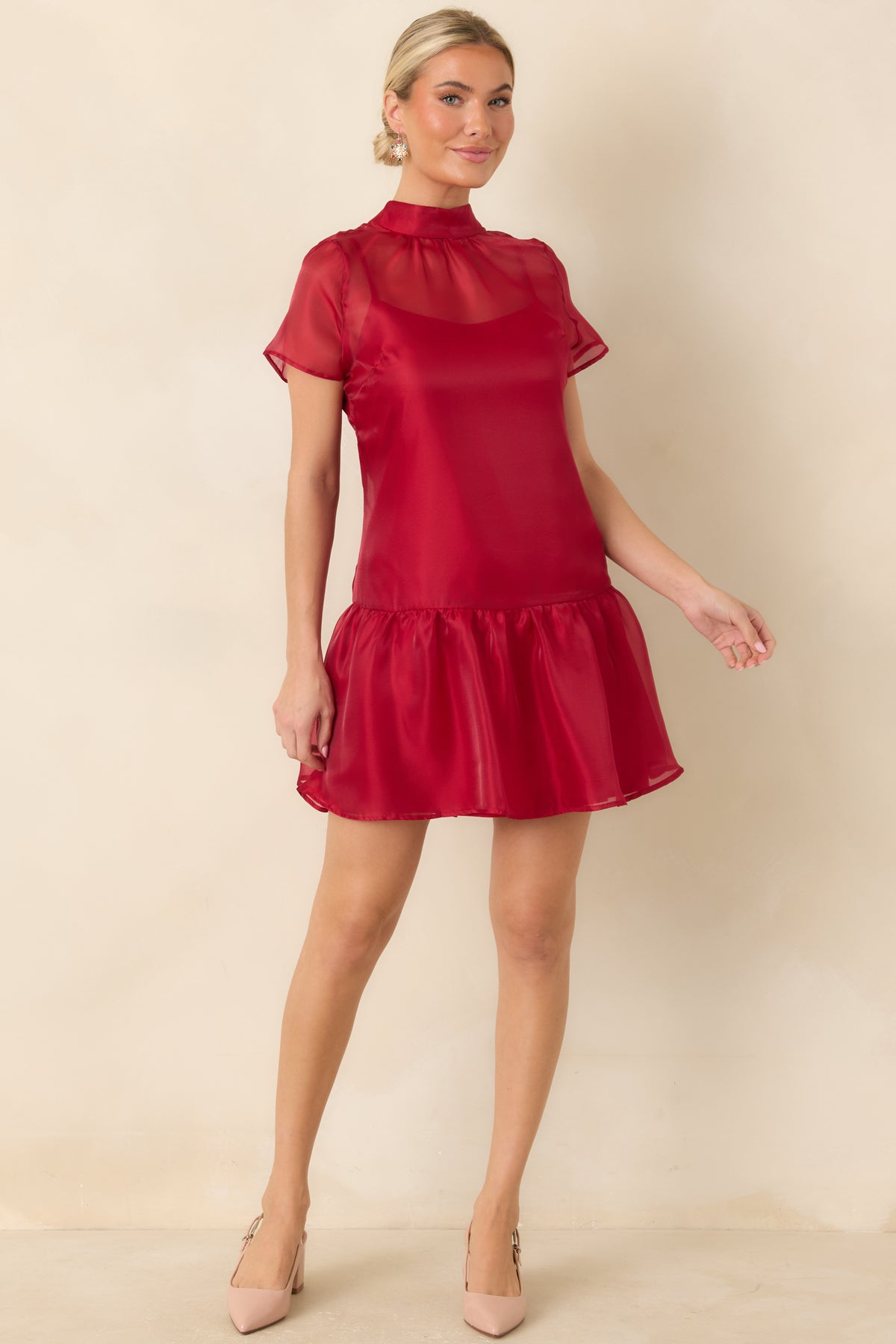 Red mini dress featuring a softly shaped silhouette, sheer upper detailing, and a playful ruffled hemline.