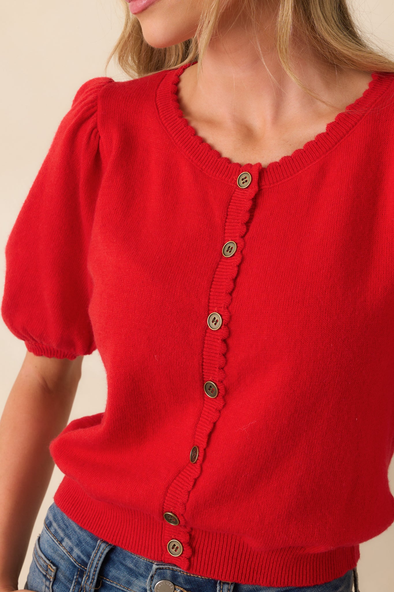 Zoomed-in image showing the knit fabric texture, scallop edging, and small round buttons at the front.