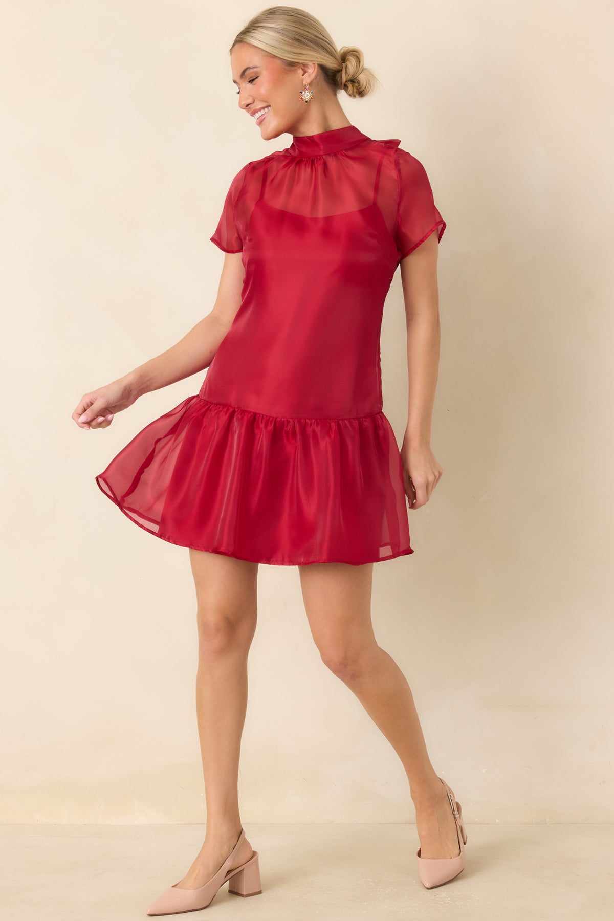 Red dress with a translucent neckline, short sheer sleeves, and a flowing skirt finished with a gathered ruffle.