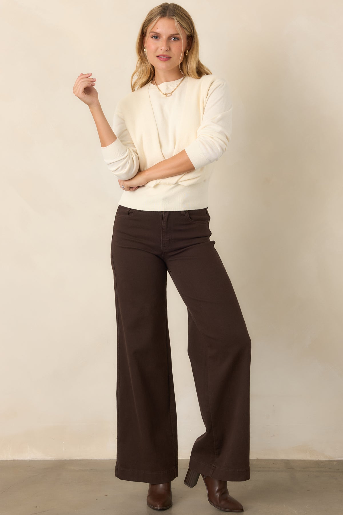 Refined layered sweater featuring a crewneck sleeveless foundation, coordinating long-sleeve overlay, front twist construction, and a structured wide ribbed hem.