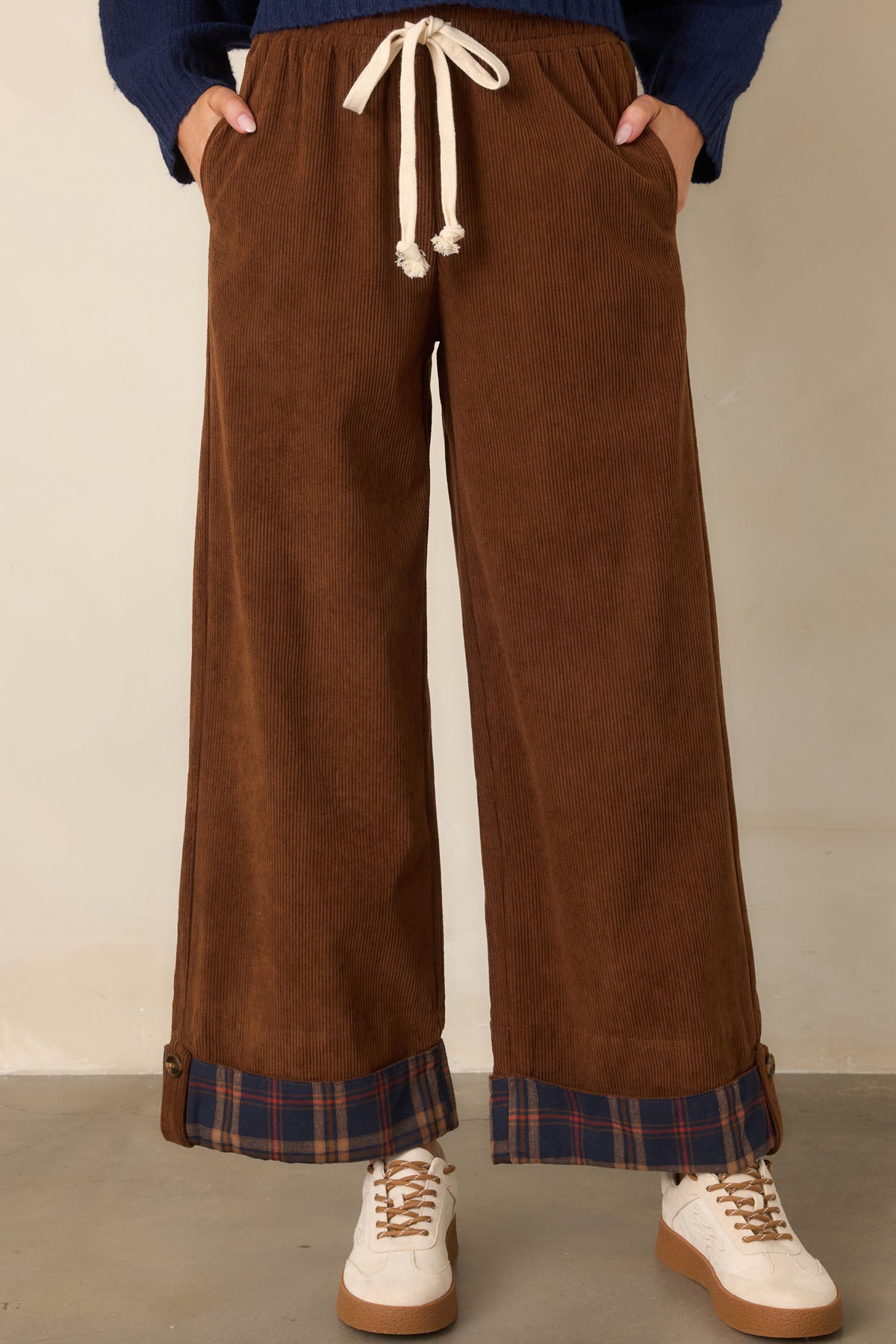 Relaxed brown wide-leg pants feature a flexible drawstring waist and patterned navy plaid hem cuffs.