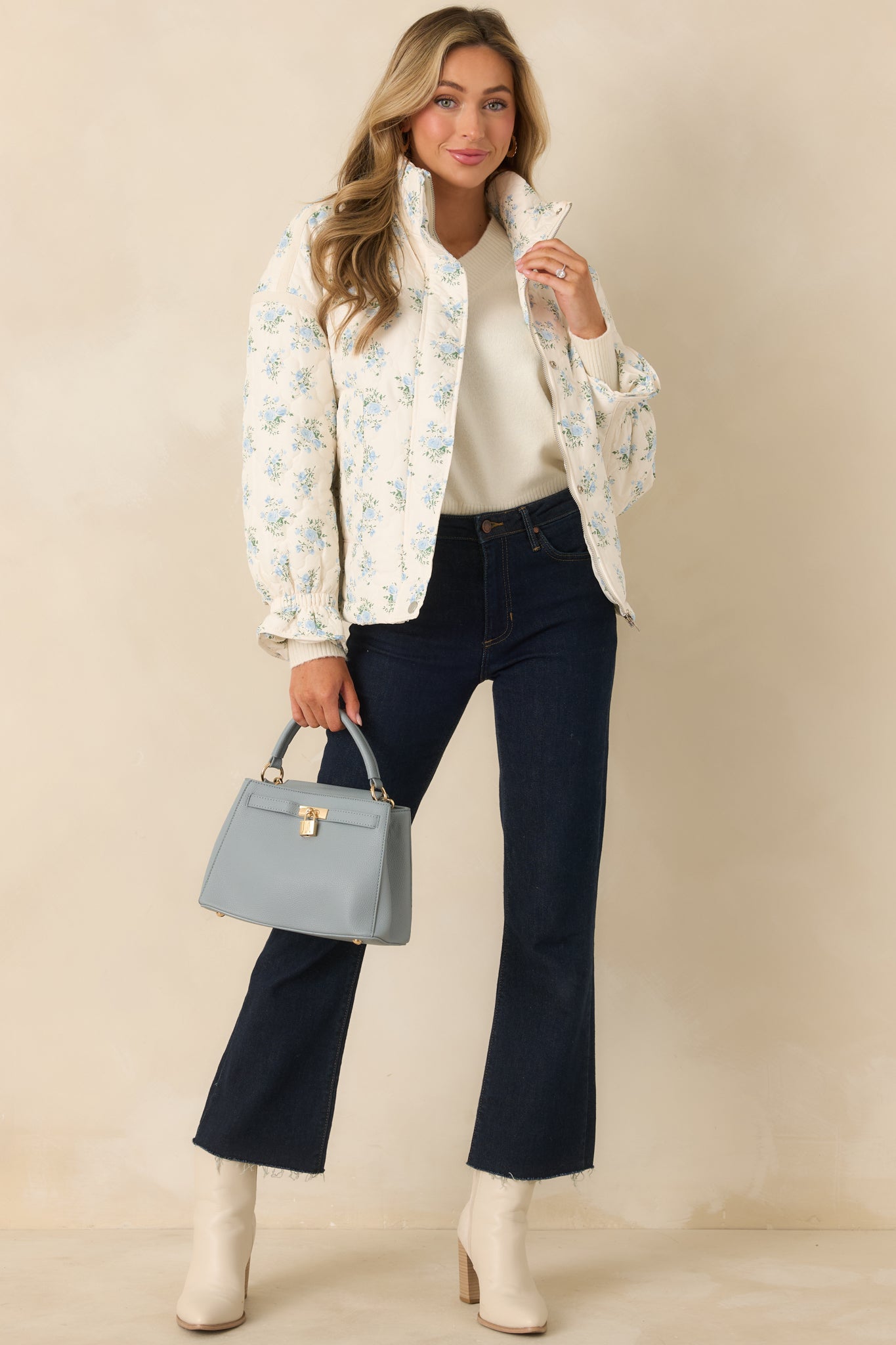 Relaxed-fit ivory quilted jacket with blue floral pattern, high neckline, full snap-front closure, and gentle structured silhouette.