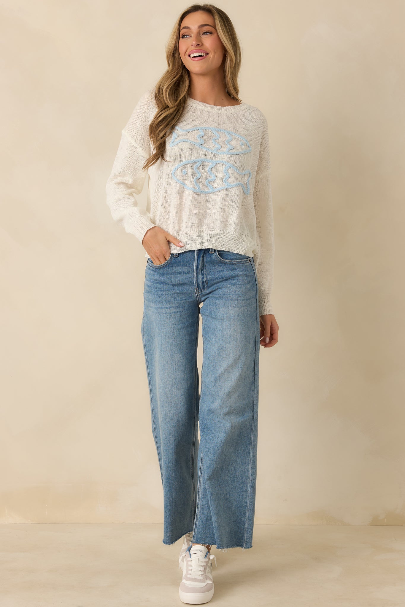 Front view of relaxed-fit ivory sweater showing embroidered fish details and crew neckline.