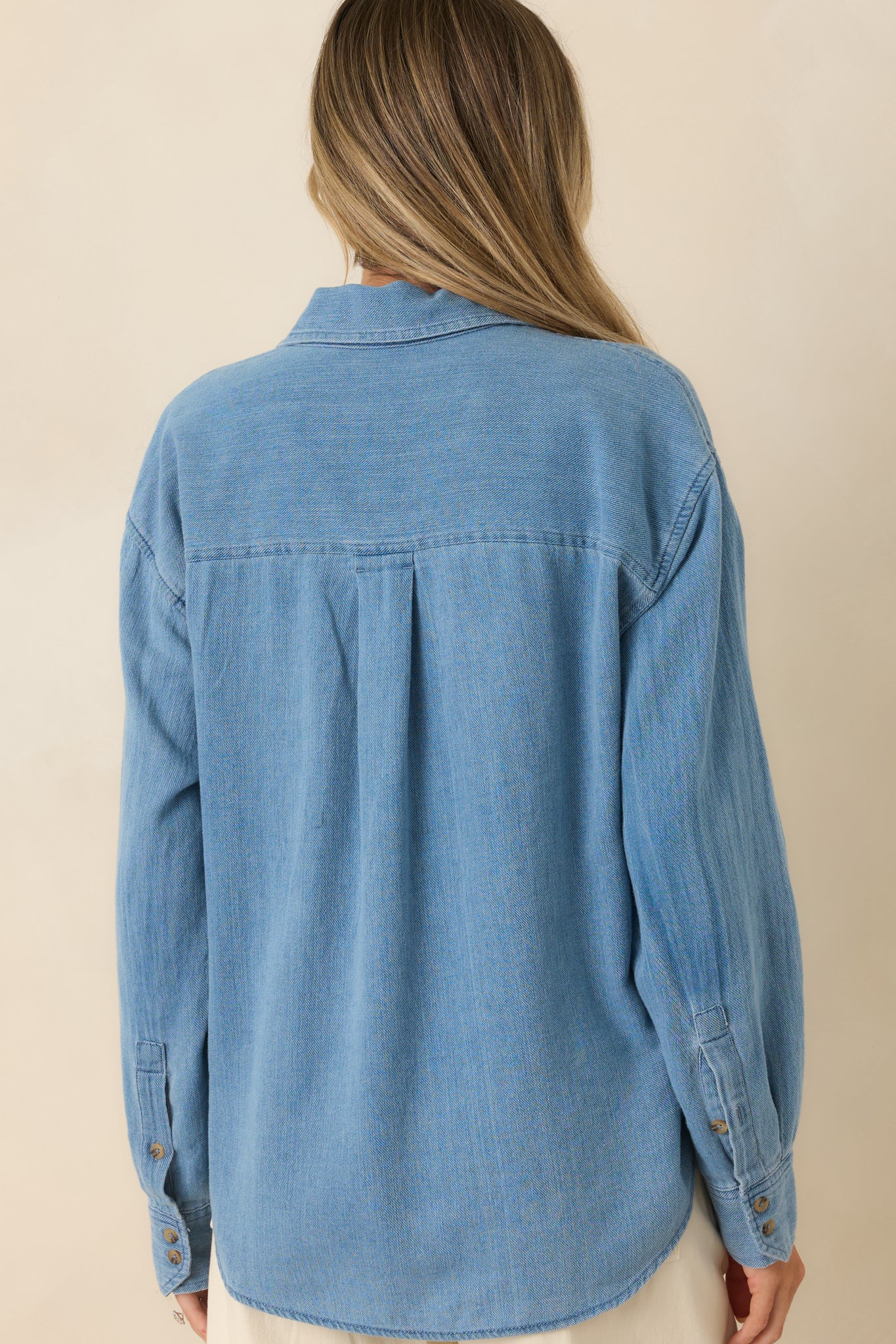 Back view of the relaxed long sleeve top highlighting the clean silhouette and curved hemline.