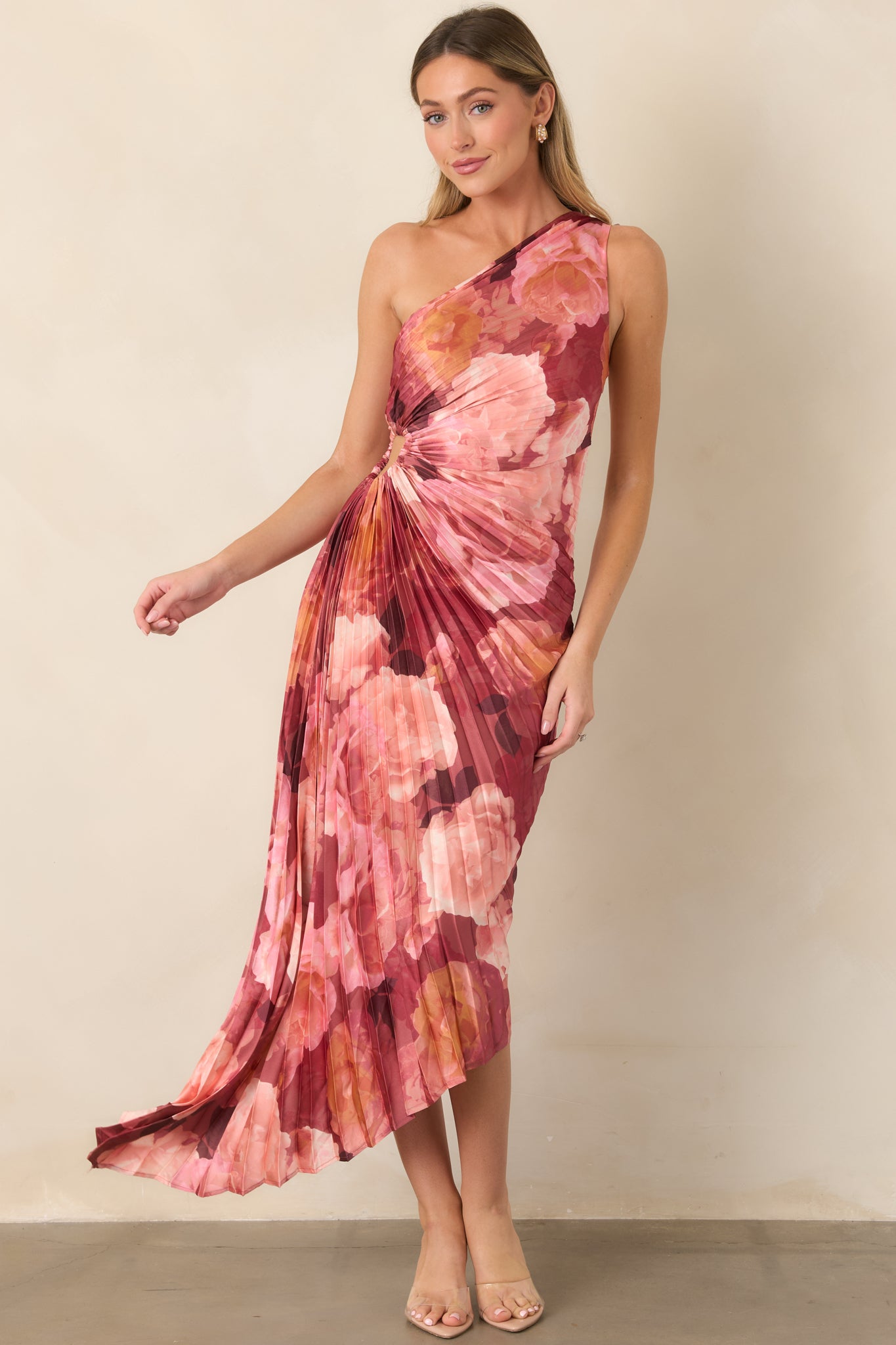 Romantic floral satin maxi dress in layered pink, rose, and burgundy tones, featuring a one-shoulder neckline, fitted waist, side cutout, allover pleating, and dramatic asymmetrical hem.