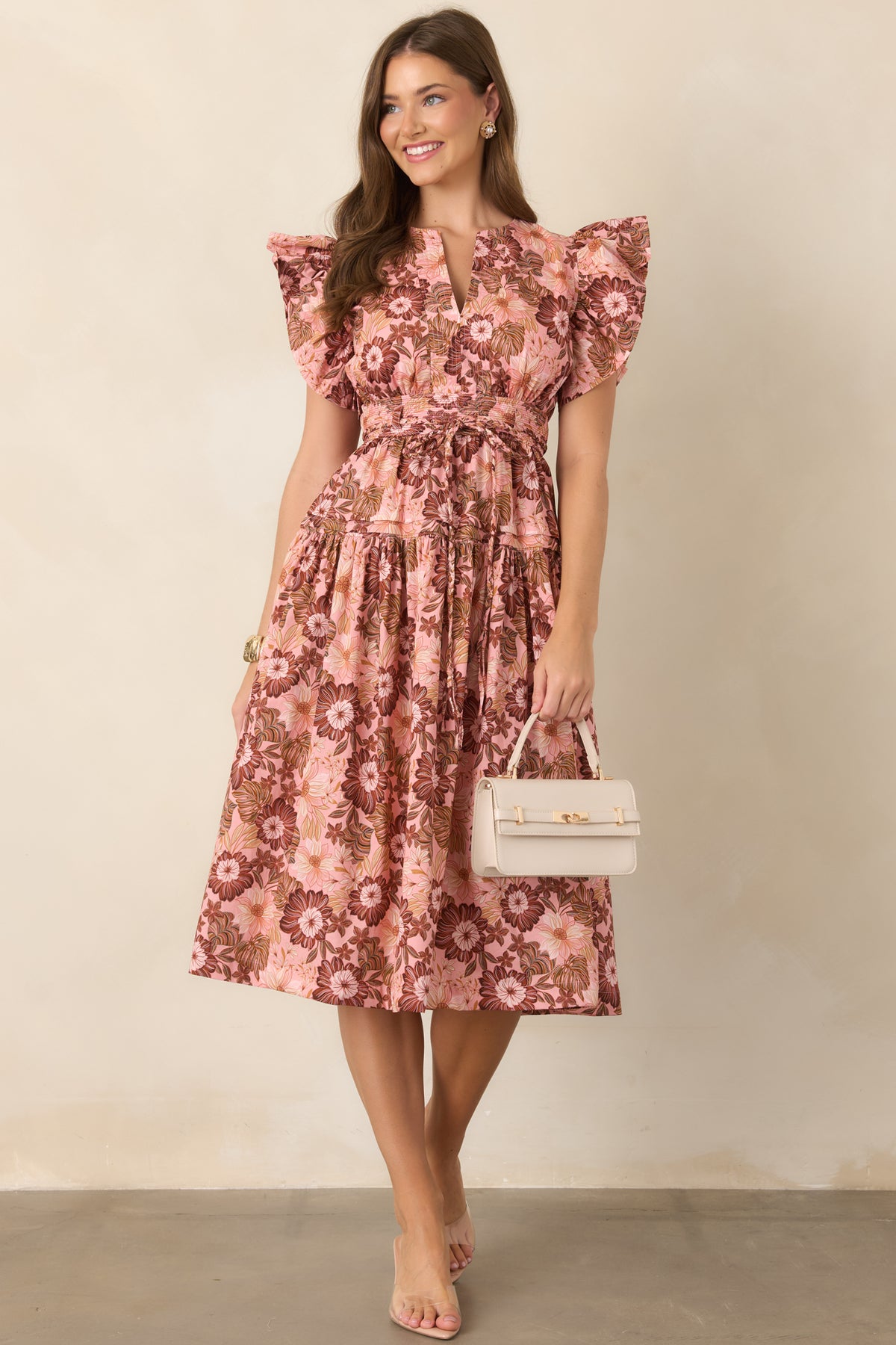 Romantic pastel pink dress covered in rich brown florals, designed with a V-neck, softly ruffled sleeves, defined waist, and flowing skirt.