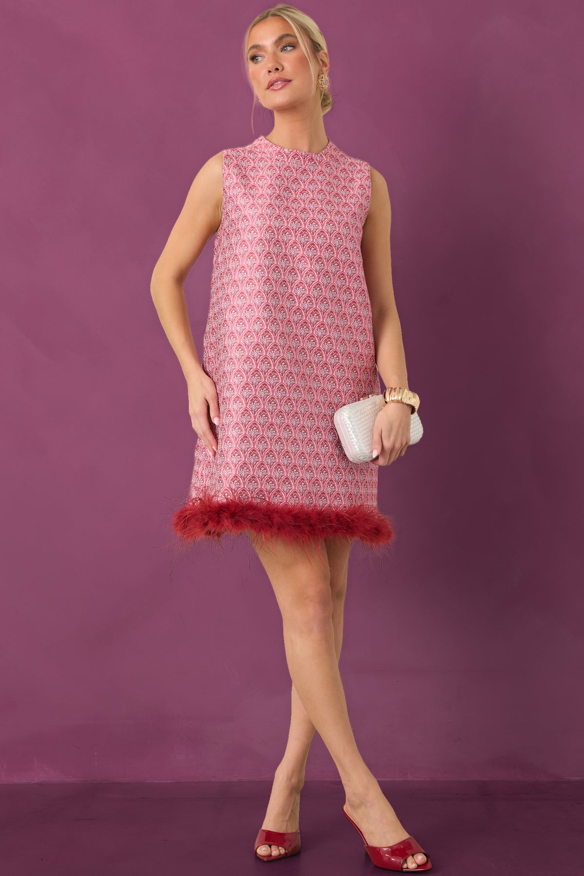 Rose pink and burgundy floral mini dress with a sleeveless silhouette, high round neckline, and wispy burgundy feather hem trim on plum background.