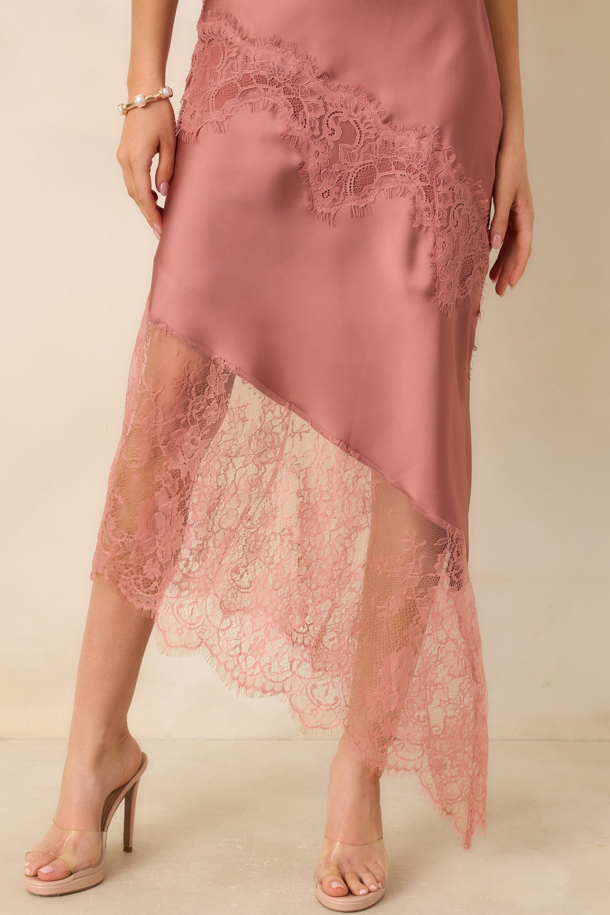 Close detail of the dress’s diagonal floral lace overlay and sheer extension along the asymmetric rose pink satin hem.