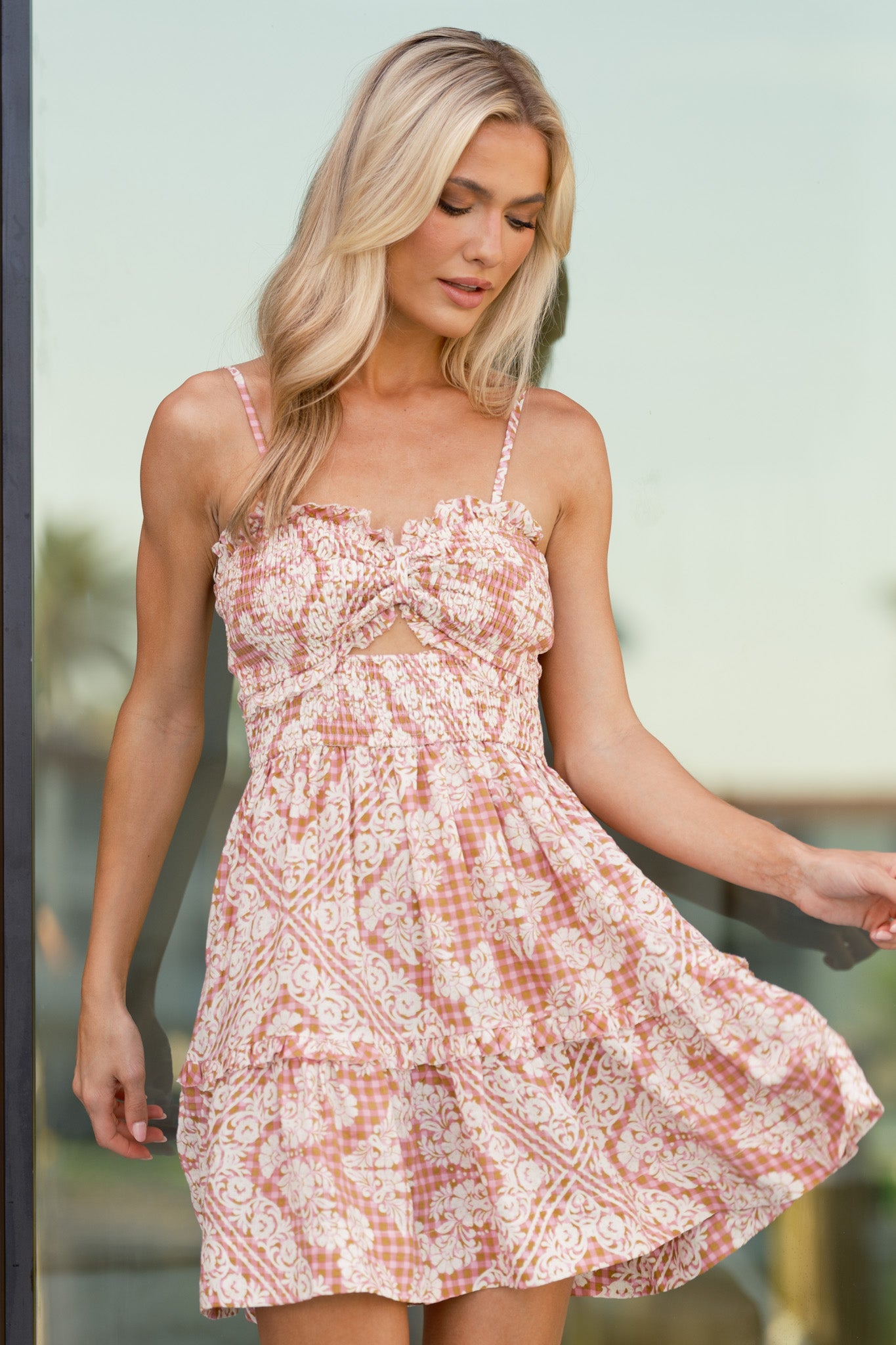 Rose pink mini dress with an ivory floral print over a pink and tan gingham base, smocked bodice, cinched sweetheart neckline, cutout detail beneath the bust, adjustable spaghetti straps, and ruffle detailing.
