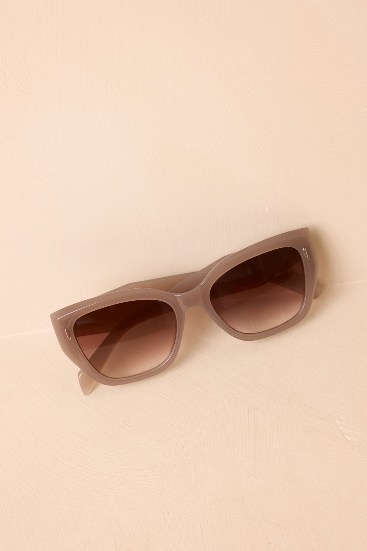 Rosy taupe sunglasses featuring wide arms, gold-tone accents, and softly lifted outer corners.