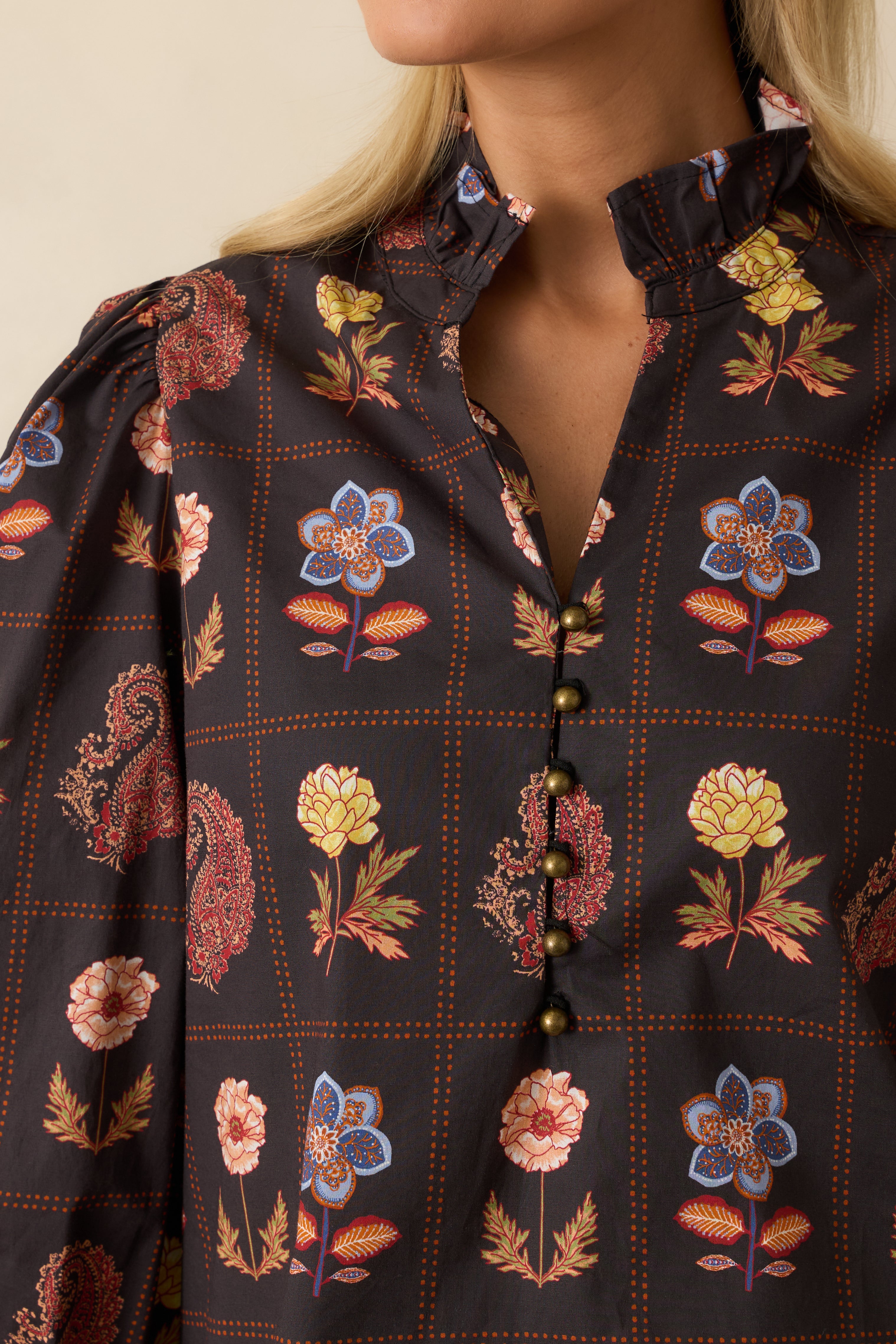 Close-up of the ruffled neckline, metallic buttons, and textured floral fabric on the black blouse.