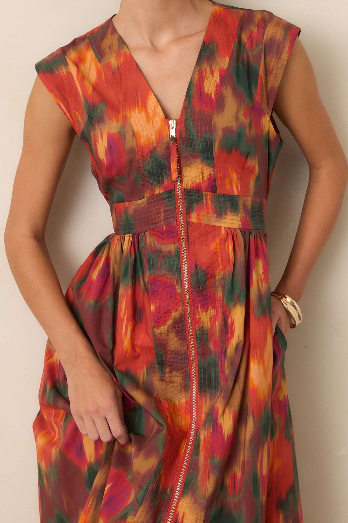 Close-up of the rust floral dress highlighting the V-neckline, painterly floral print, and polished gold-tone front zipper.