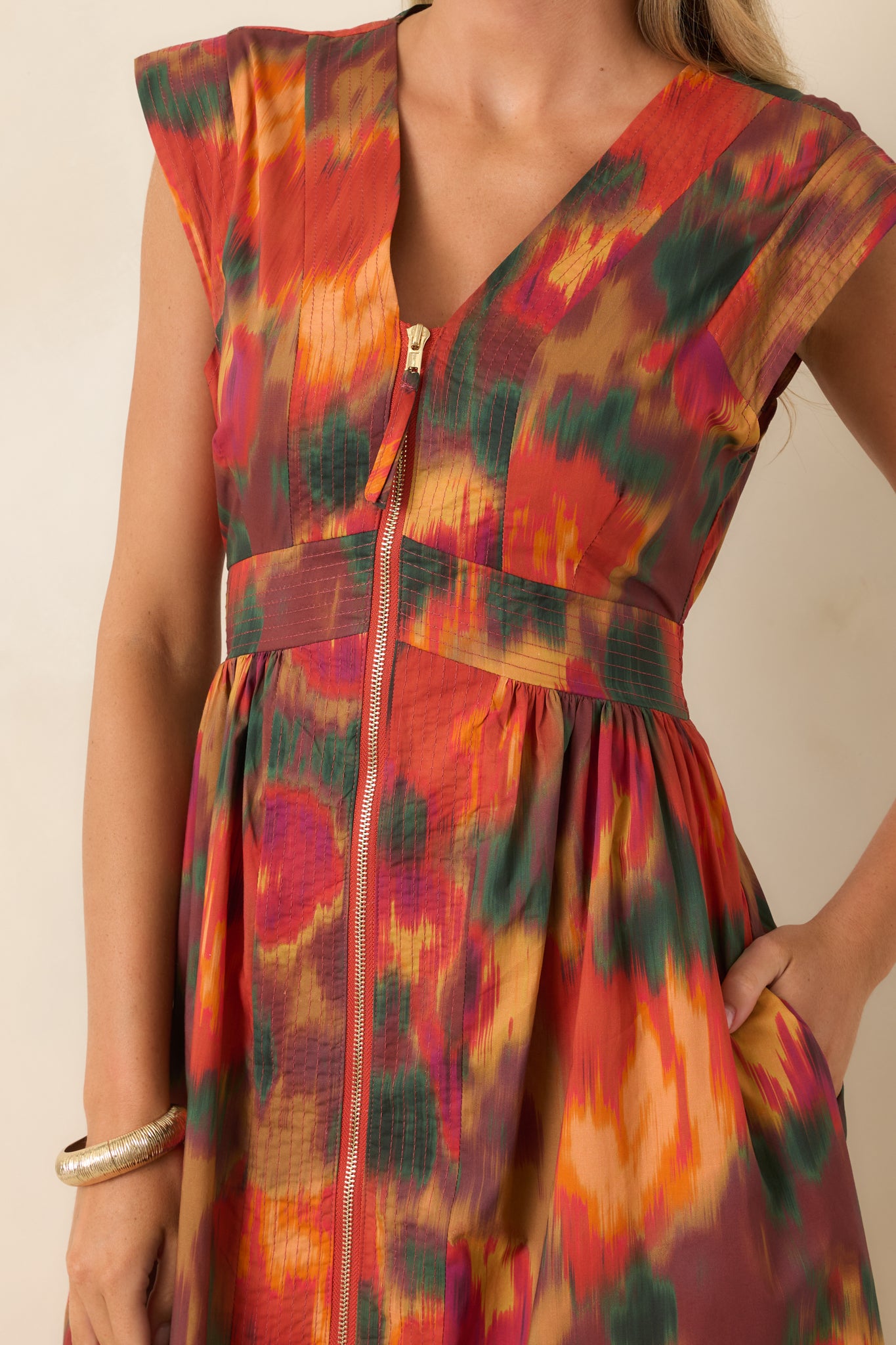Close-up of the rust floral dress highlighting the painterly multicolor print, V-neckline, fitted bodice, and polished gold-tone zipper detail.