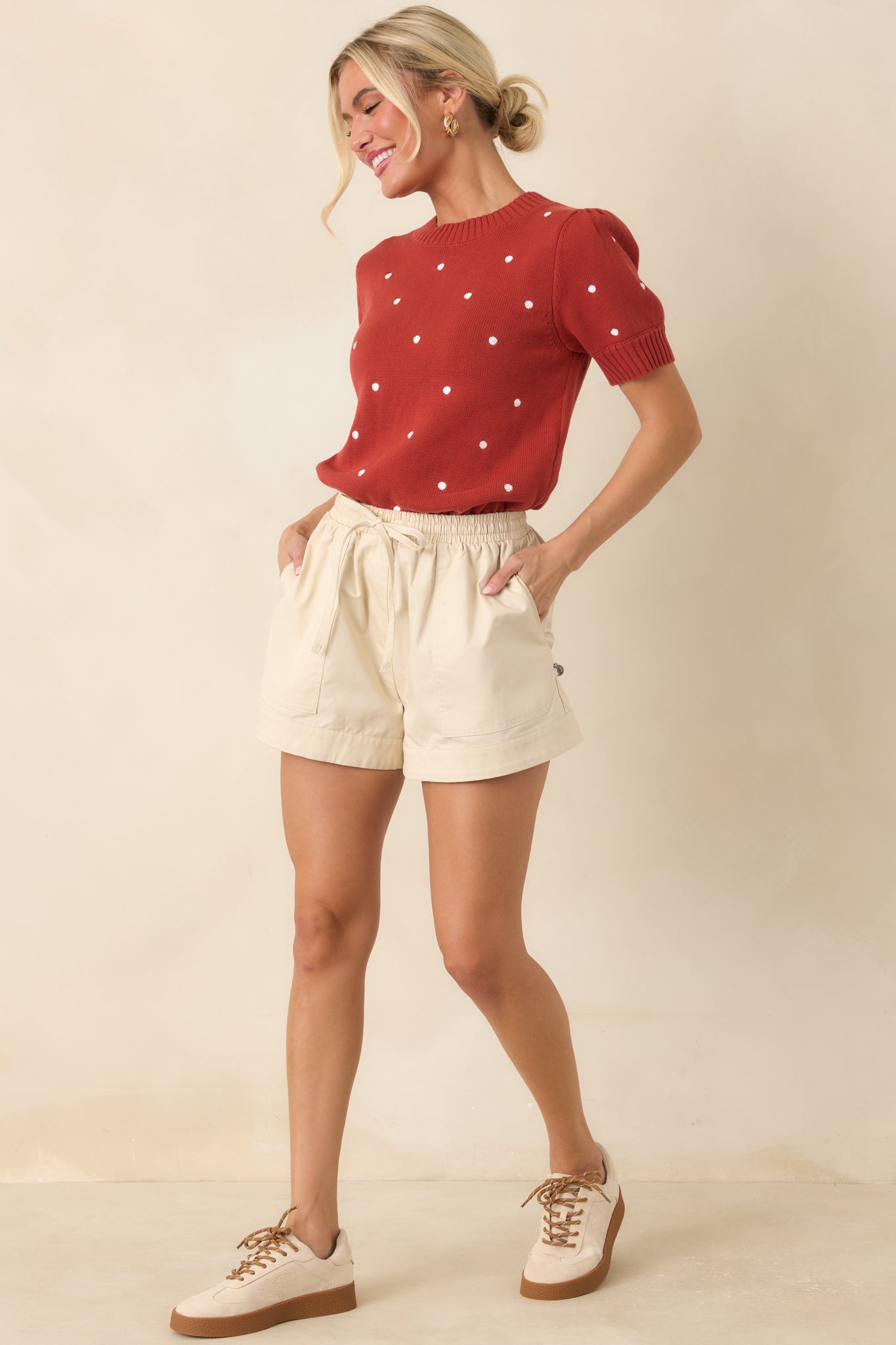 Rust red cotton knit top featuring ivory polka dots, a ribbed crew neckline, short puff sleeves, and a softly structured silhouette.