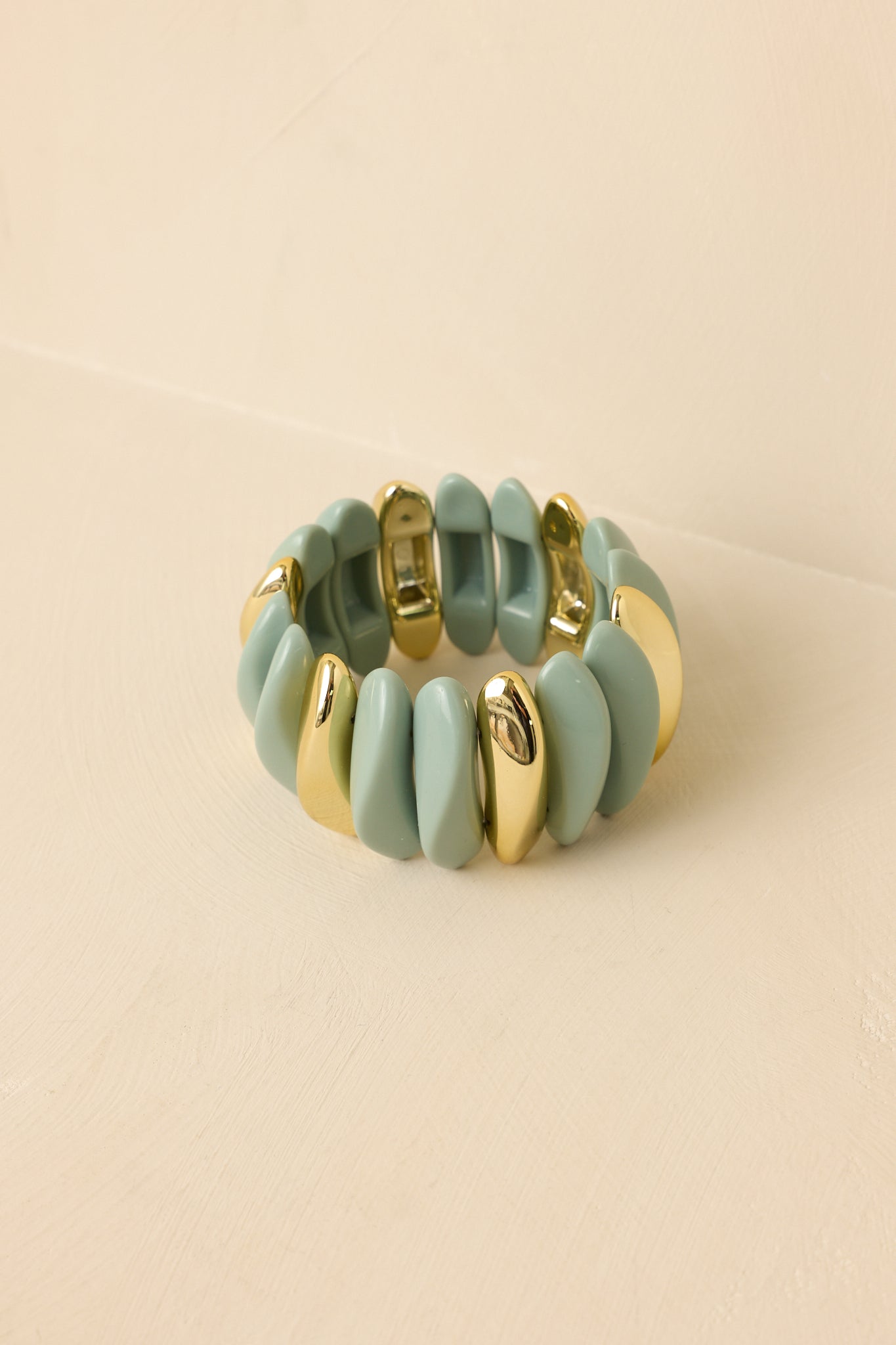 Sage green stretch bracelet featuring sculptural contoured links, gold accents, and an abstract design.
