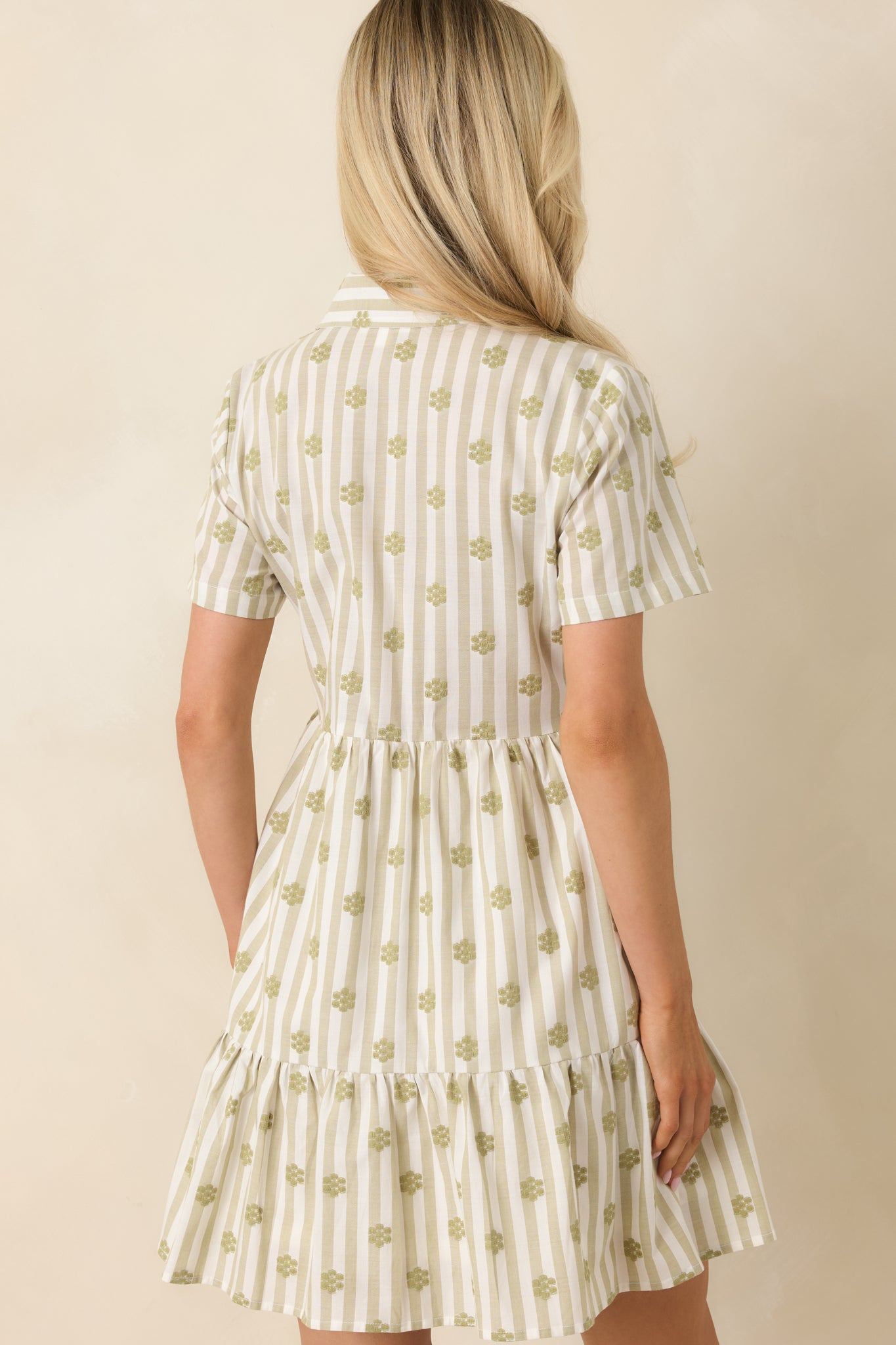 Sage green cotton mini dress showing the back of the tiered skirt silhouette with embroidered floral detailing and relaxed fit.