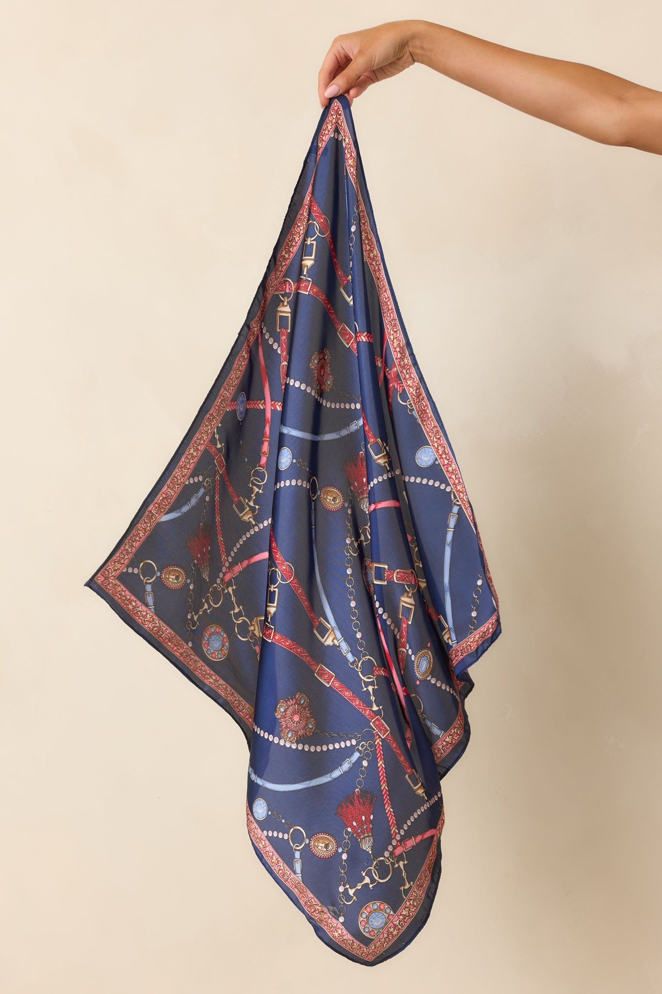 Satin hair scarf featuring an ornate print of chains, tassels, medallions, and buckle motifs in red, light blue, and gold.