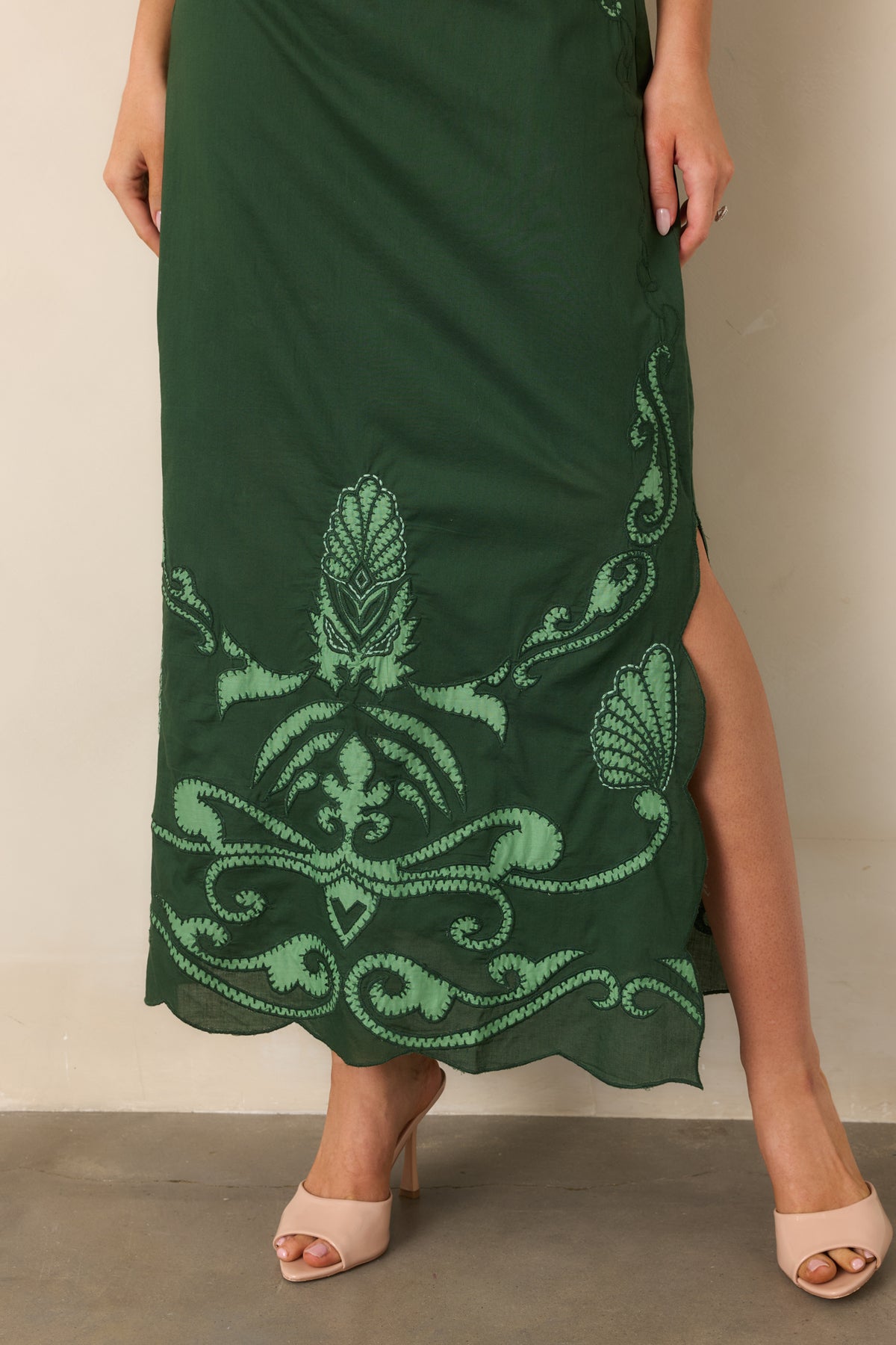 Close view of the scalloped midi hem, light green scrollwork motifs, and decorative stitching.