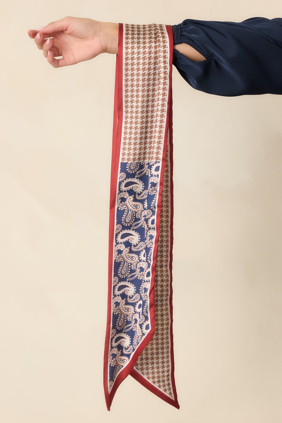 Navy paisley and taupe houndstooth scarf with red borders and pointed ends, draped over an arm.