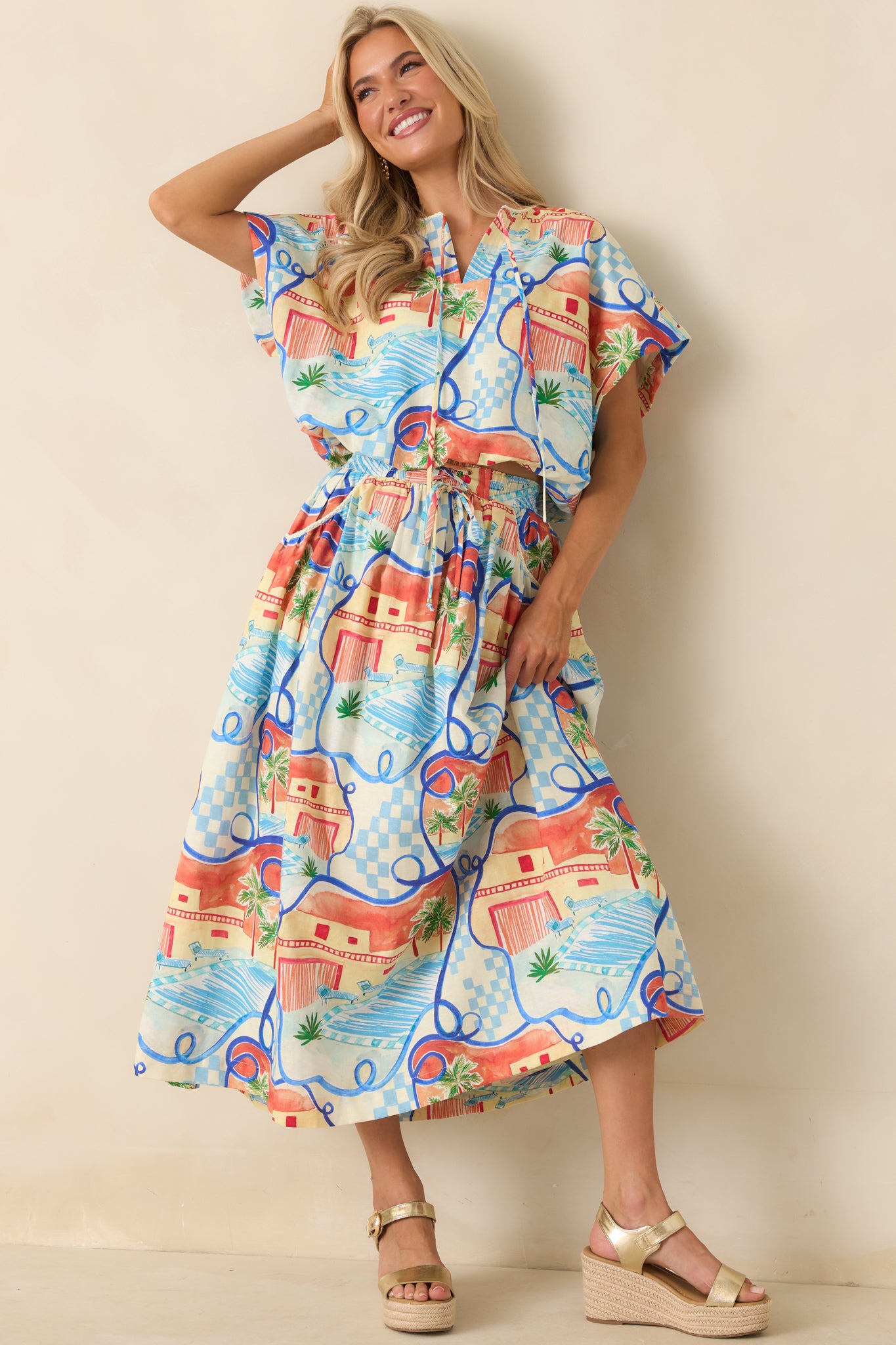 Scenic print top featuring palm trees, poolside views, coastal architecture, and a relaxed silhouette with dolman sleeves.