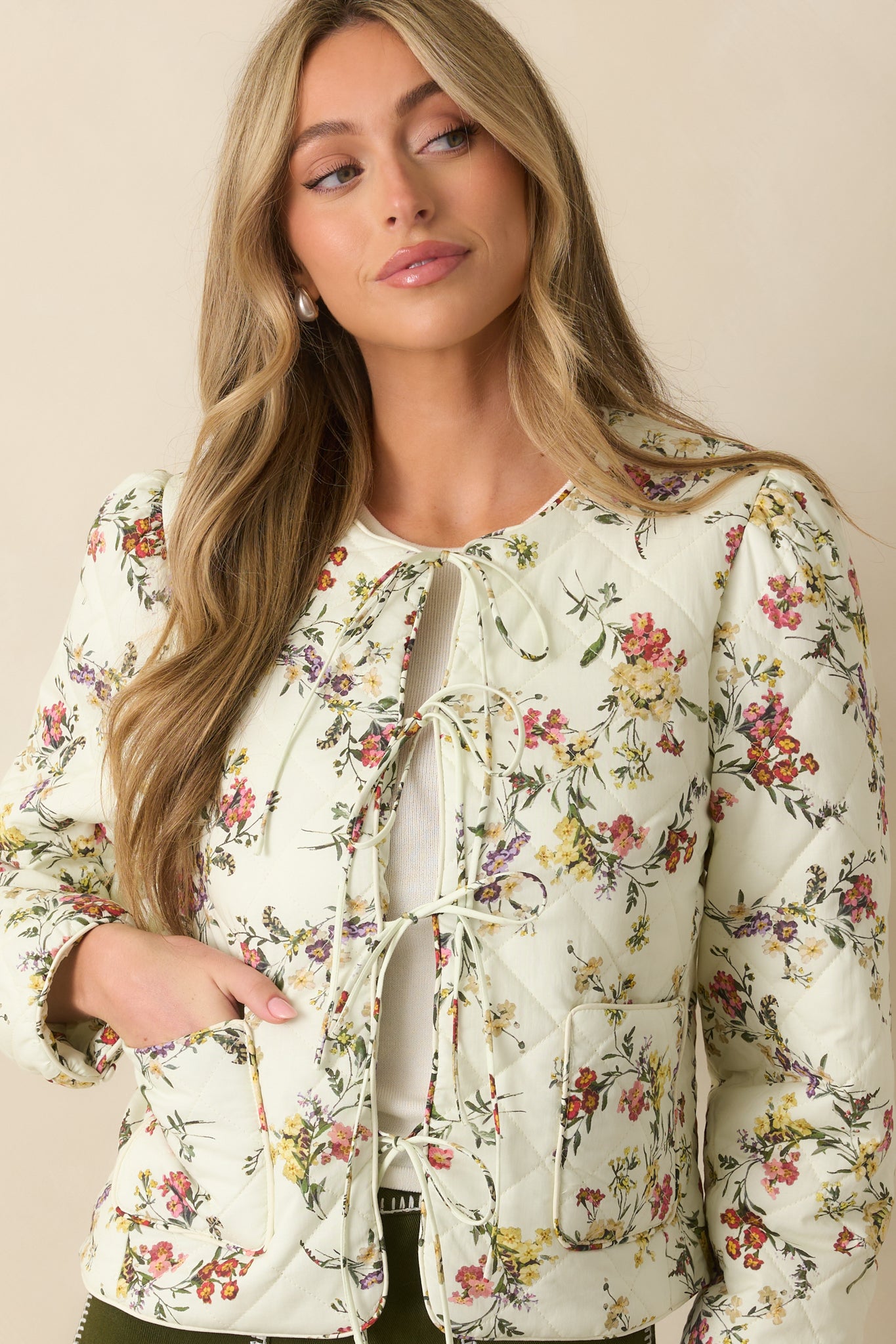 Close view of the self-tie bow and floral print details on the ivory jacket.