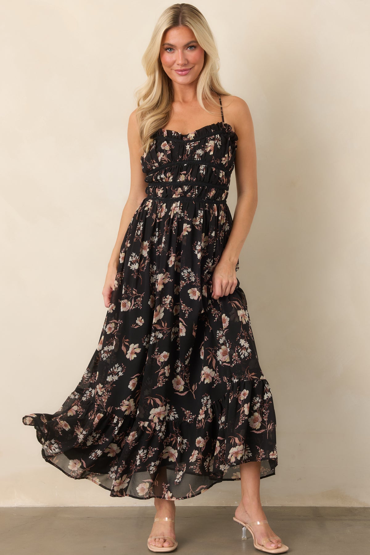 Sheer black floral dress with slender straps, ruffled neckline, gathered bodice, and a softly cascading ruffled hem.