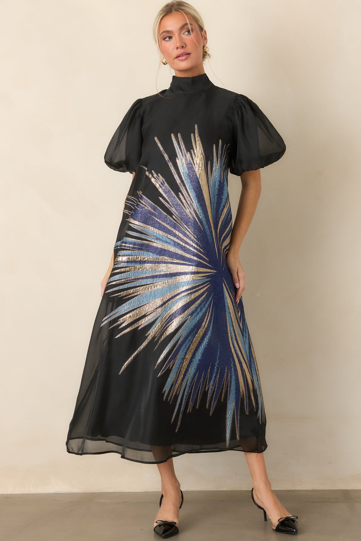 Sheer black midi dress with a shimmering blue and gold metallic starburst design and sheer puff sleeves.