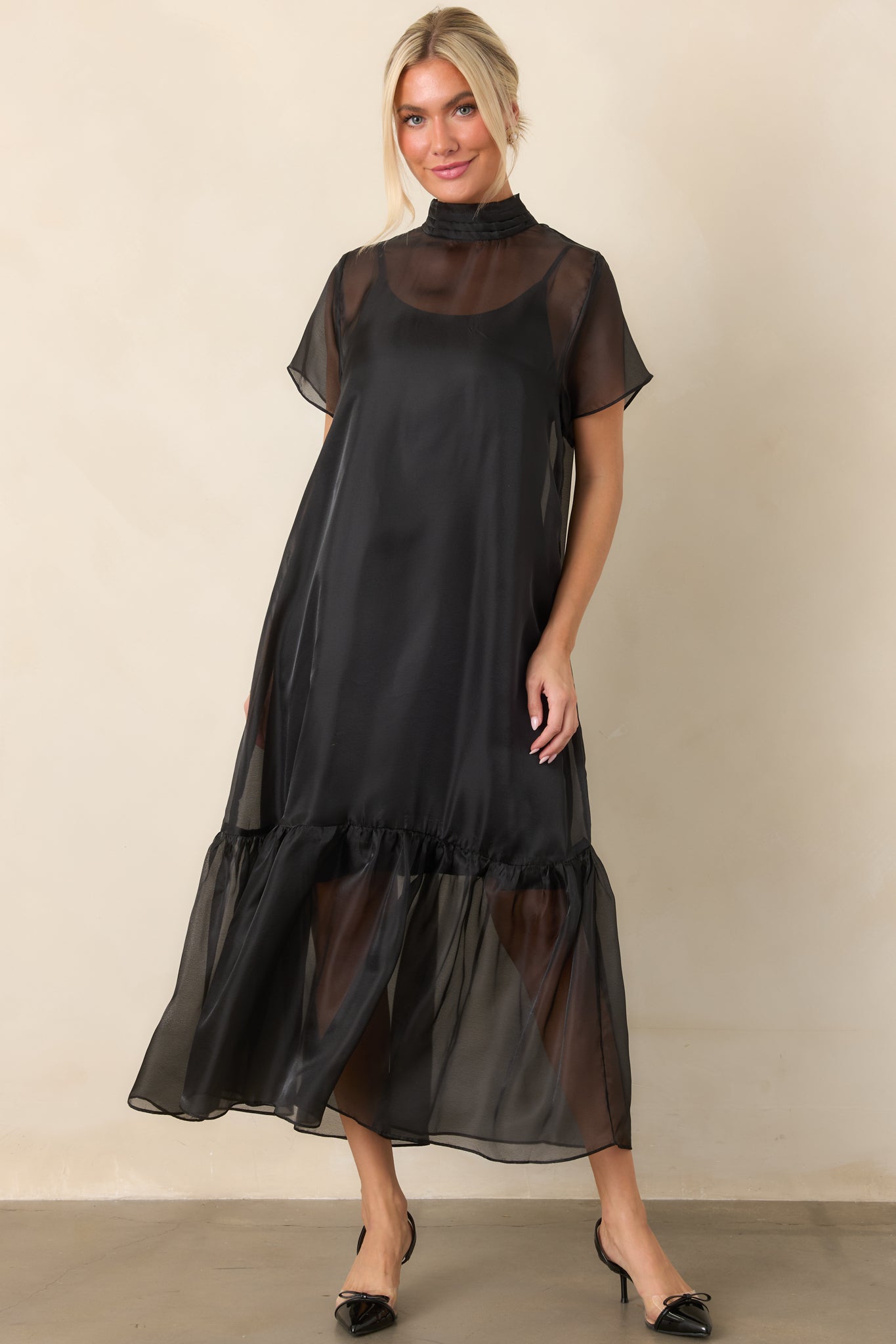 Flowing sheer maxi silhouette with a refined mock neckline, short organza sleeves, and a textured ruffle finish along the hem.
