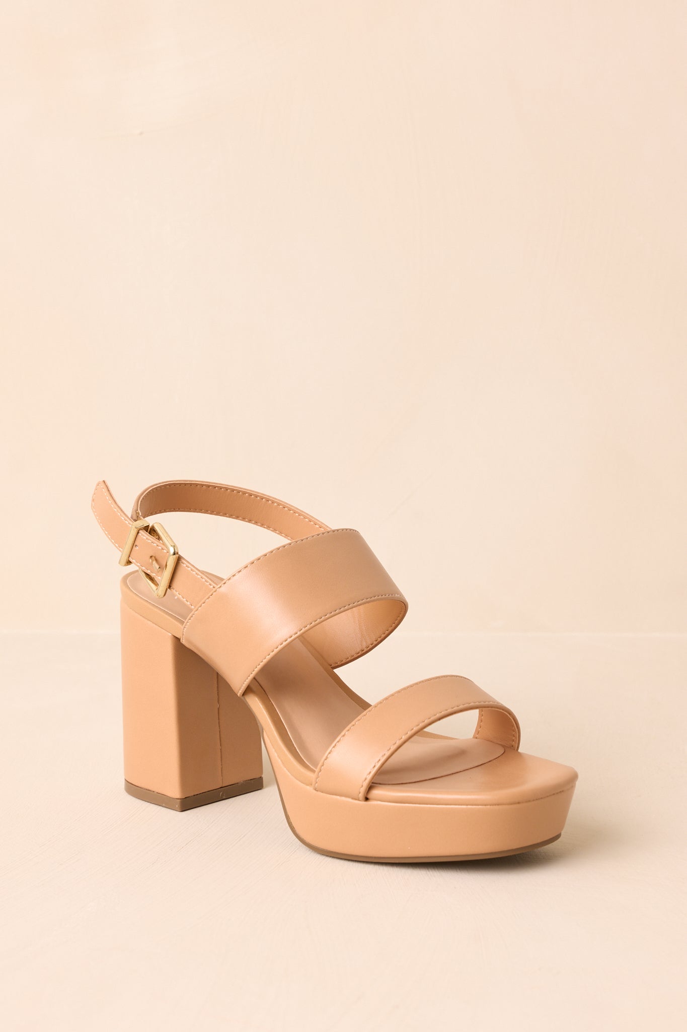 Angled view of the shoes against a beige background, showcasing the ankle strap and buckle closure.
