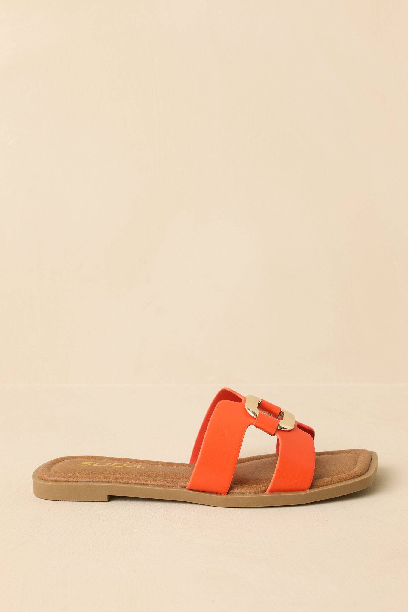 Side angle of orange flat slide sandals displayed on a beige background, emphasizing the low-profile sole and strap placement.