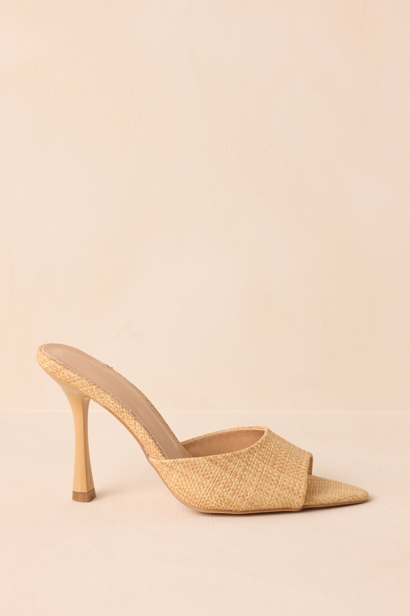 A side cropped view of the mule, focusing on the sleek stiletto heel and natural-colored raffia upper.