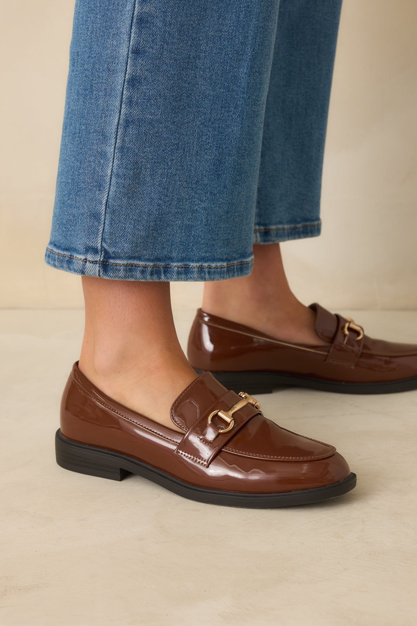 Side-focused cropped image of brown loafers showing the gold-tone horsebit detail on the vamp.