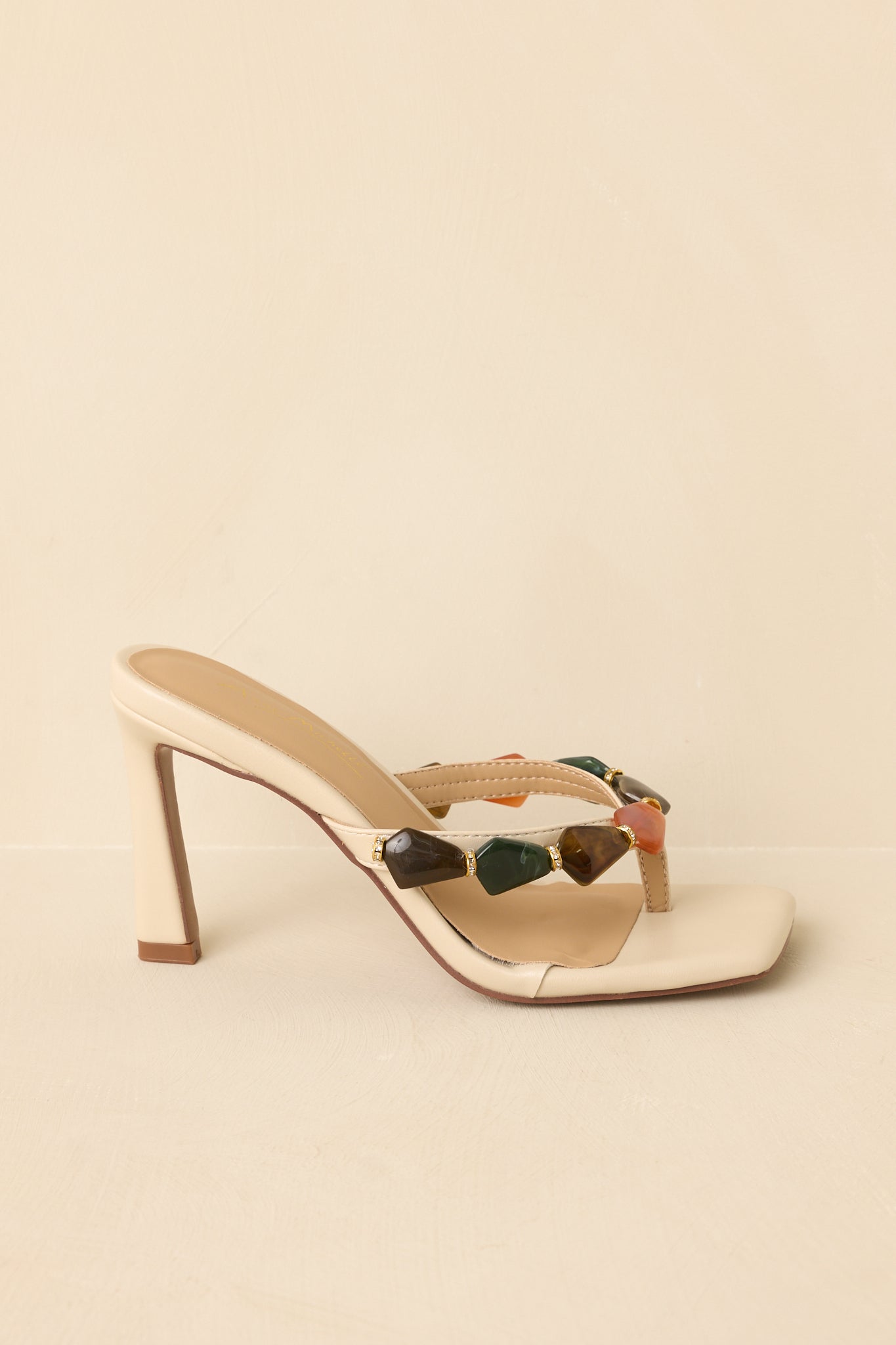 Side profile of heeled sandals on beige background showing sturdy heel and clean, modern lines
