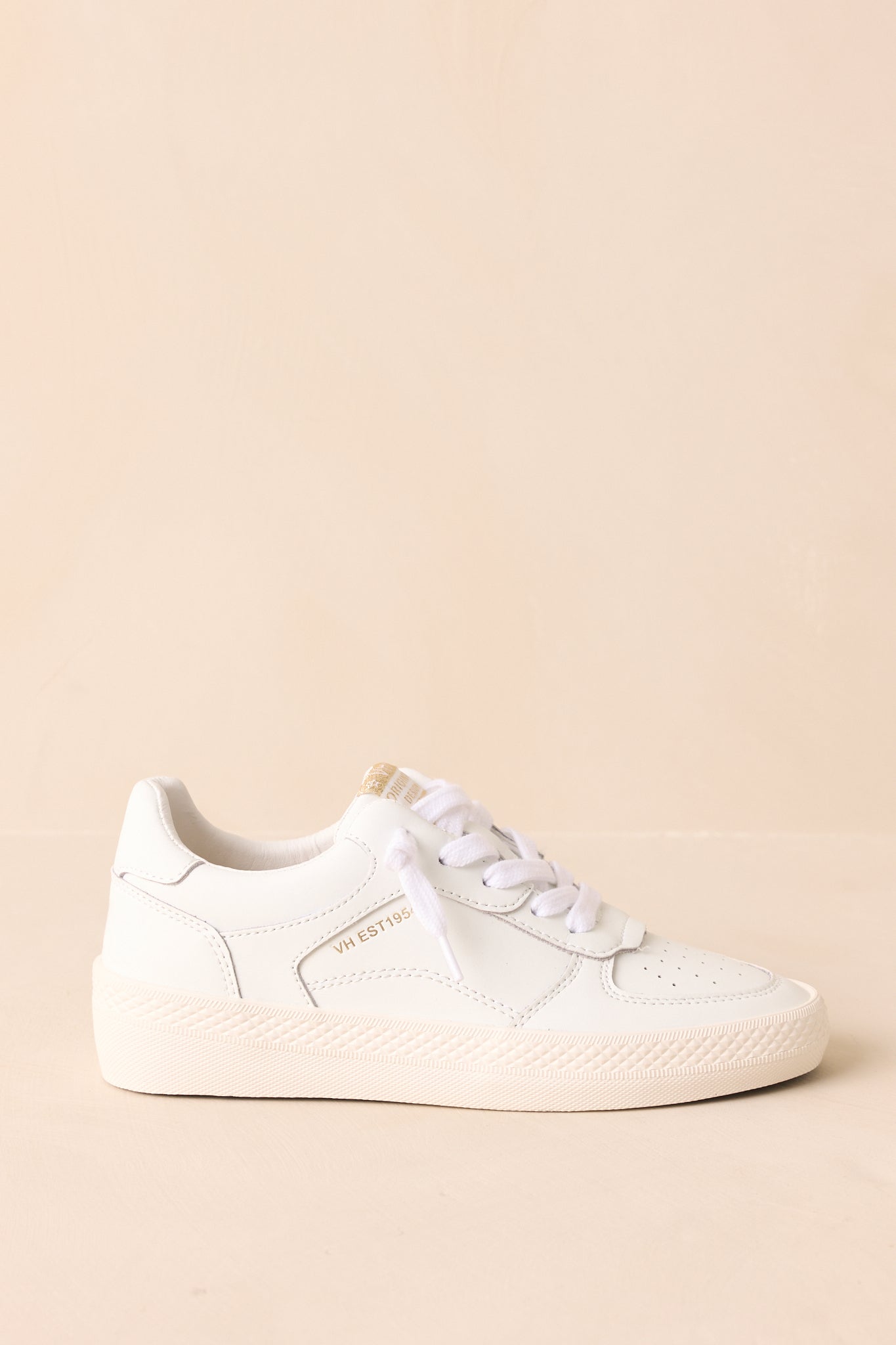 Side view of white distressed sneakers highlighting the textured leather and gold logo detailing on the tongue.