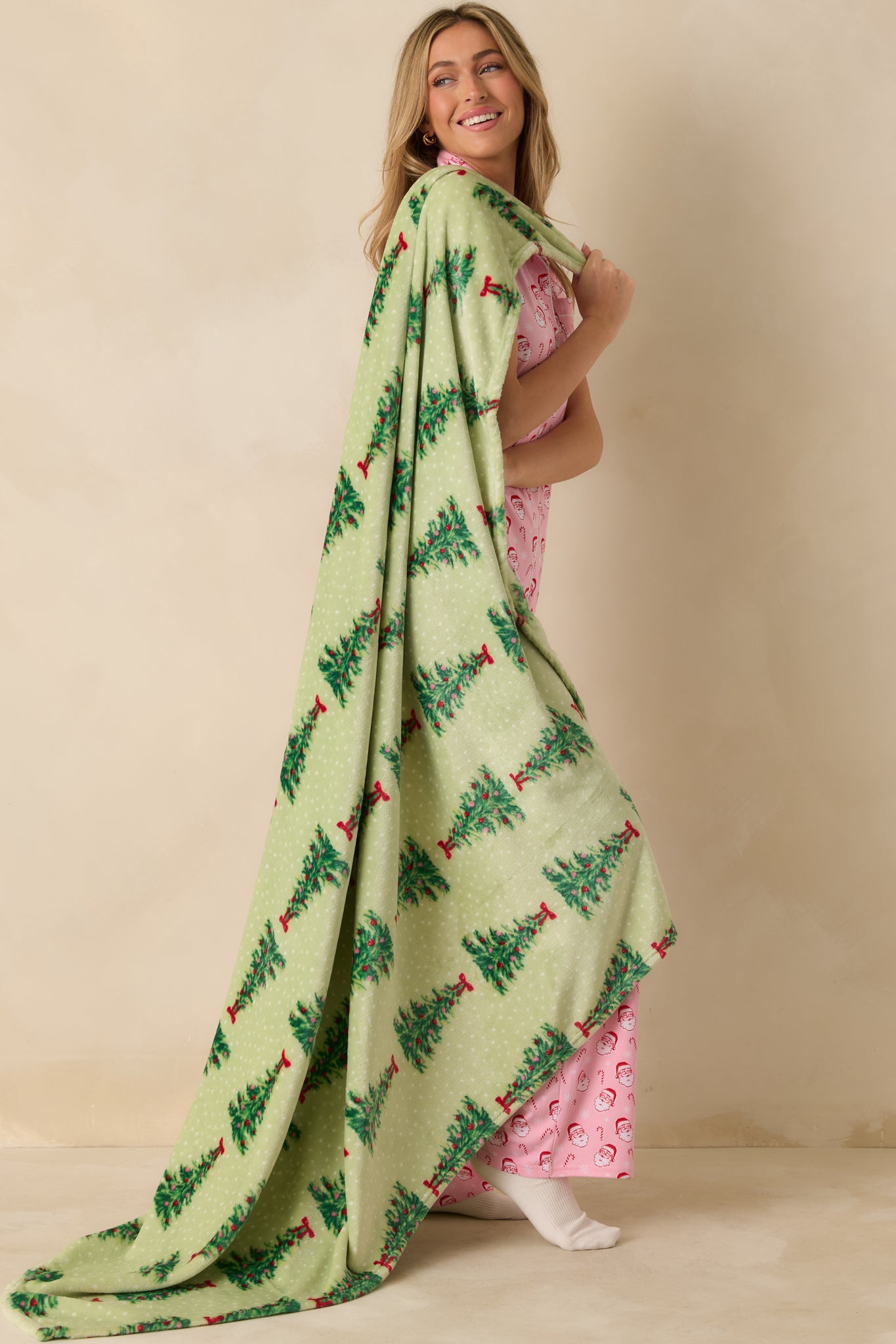 Side view of the light green throw blanket featuring allover Christmas tree print with red bows and ornaments.