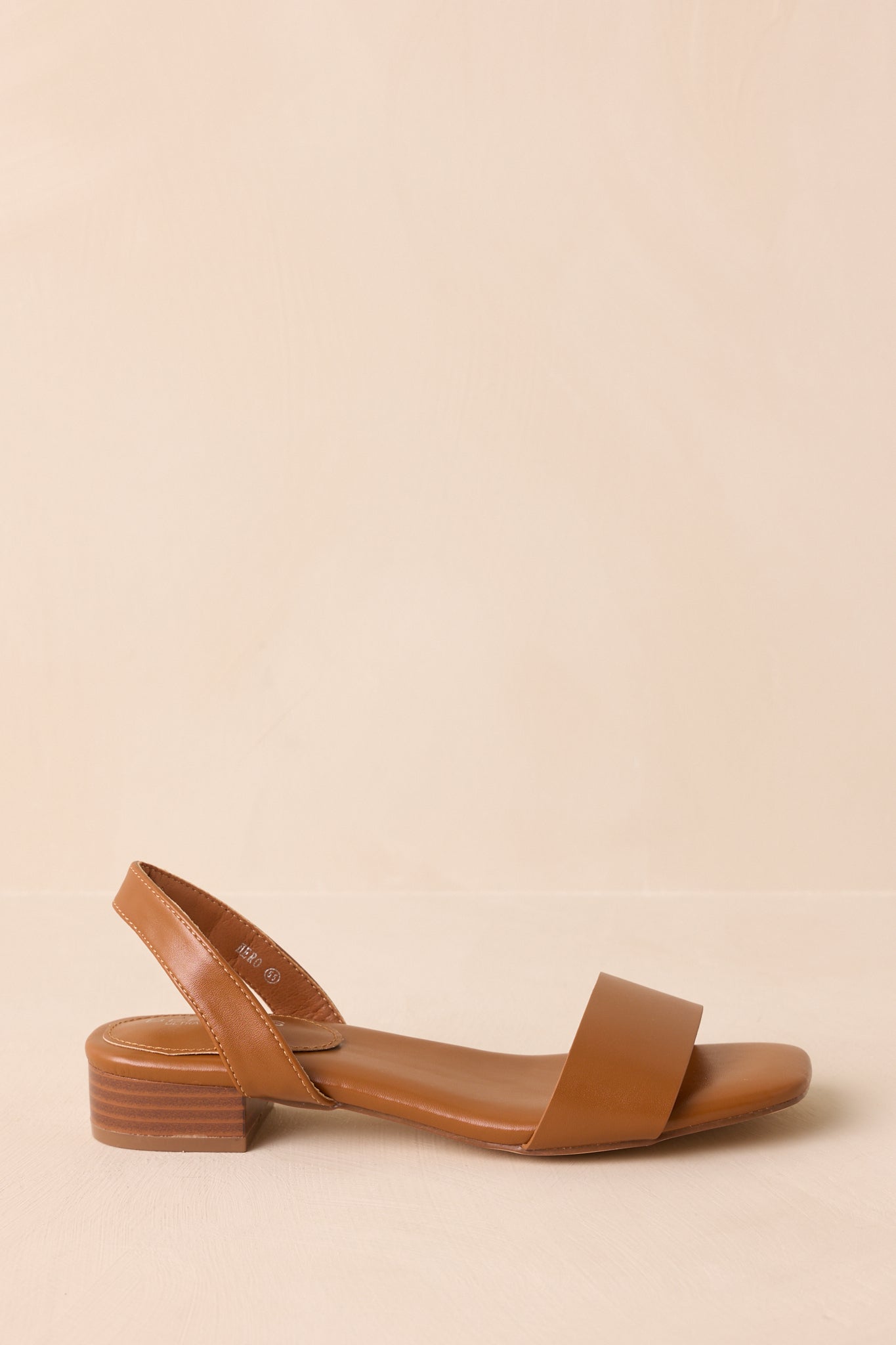 Side view of caramel brown sandal highlighting flat sole and single toe strap.
