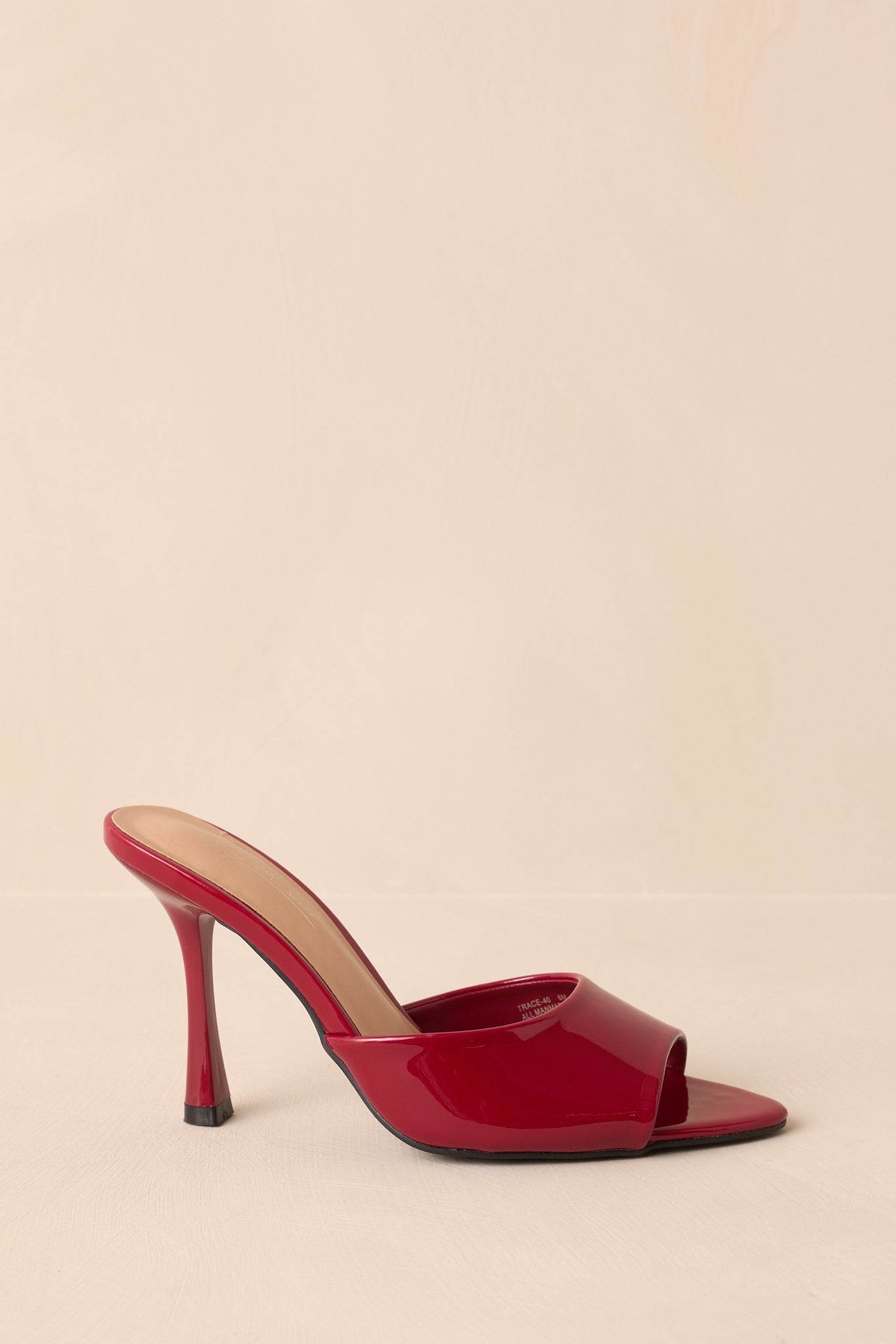 Side view of red stiletto mule heels on a beige backdrop.