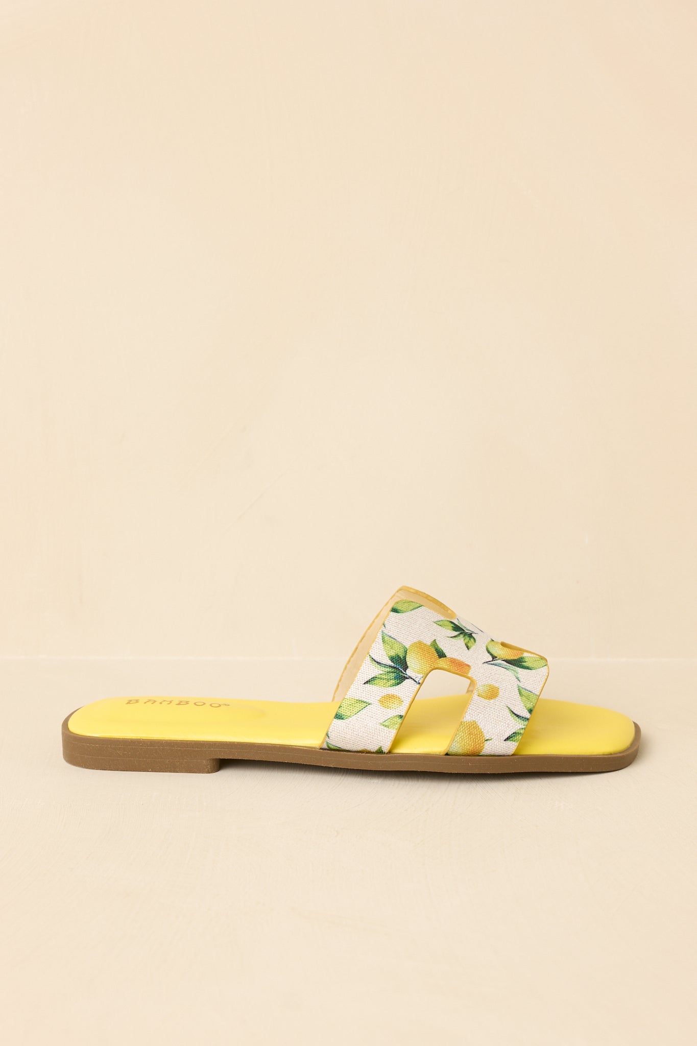 Side view of slide sandals on beige background showing low-profile flat sole and wide printed strap