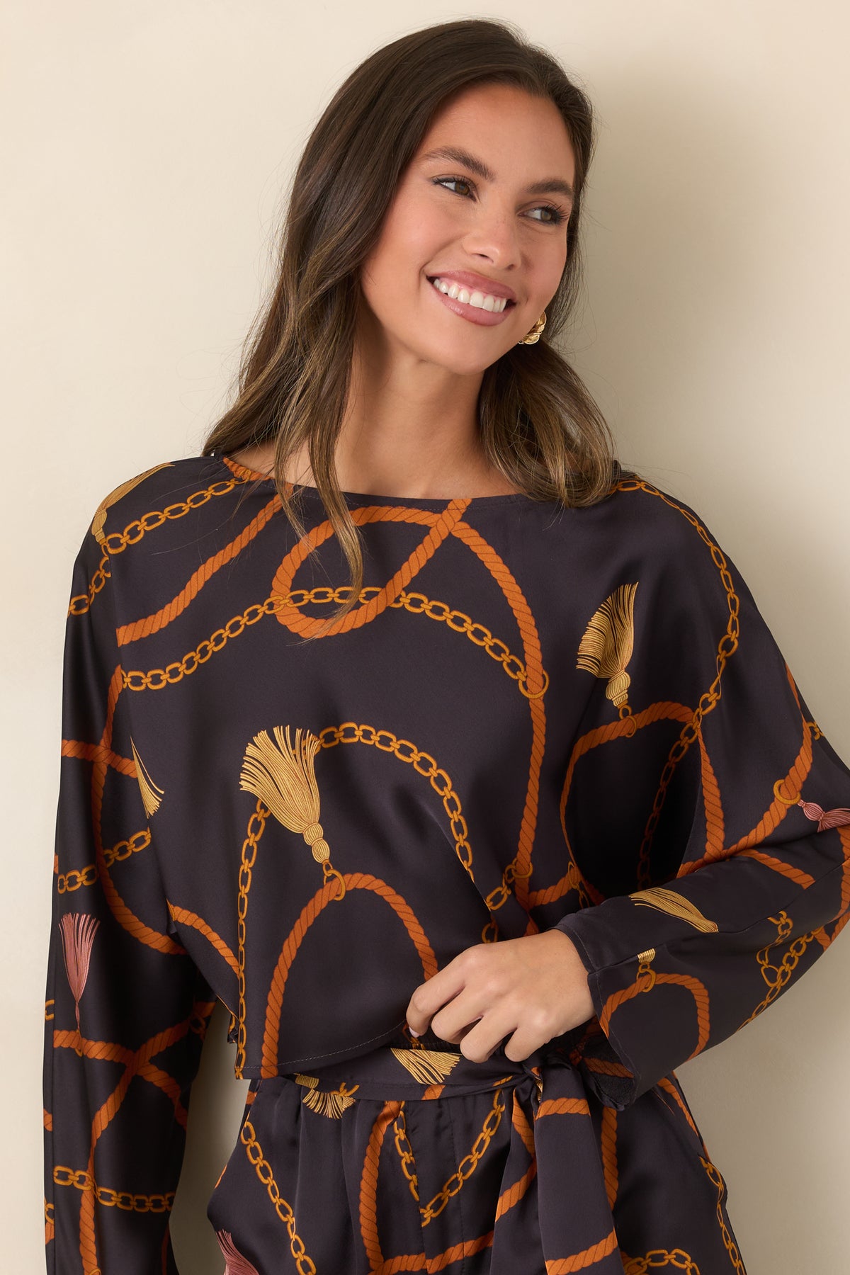 Silky black cropped top featuring interwoven rust ropes, gold chains, and decorative tassel accents.