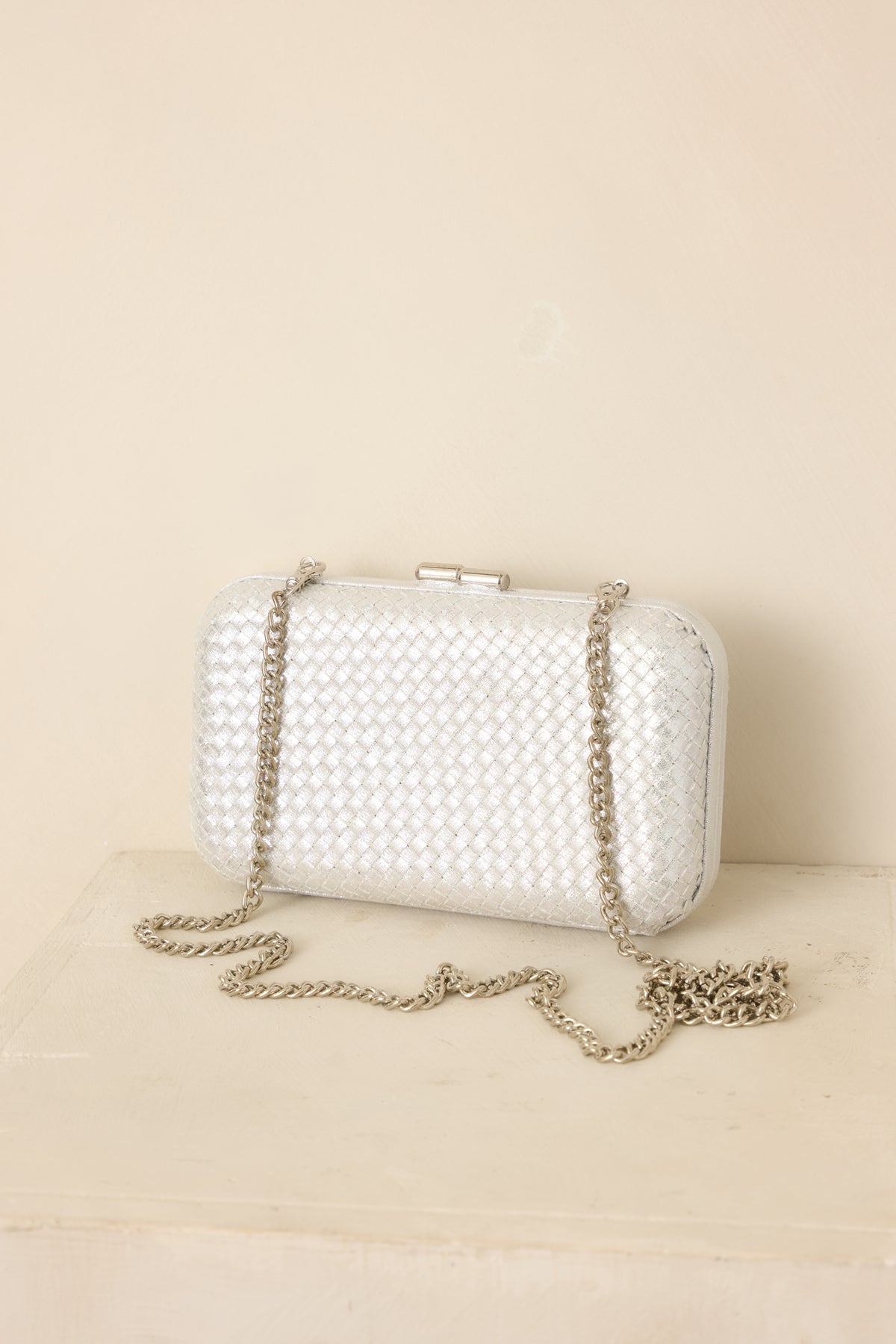 Structured silver clutch showcasing a textured woven design, hinged frame, top clasp closure, and detachable chain strap.