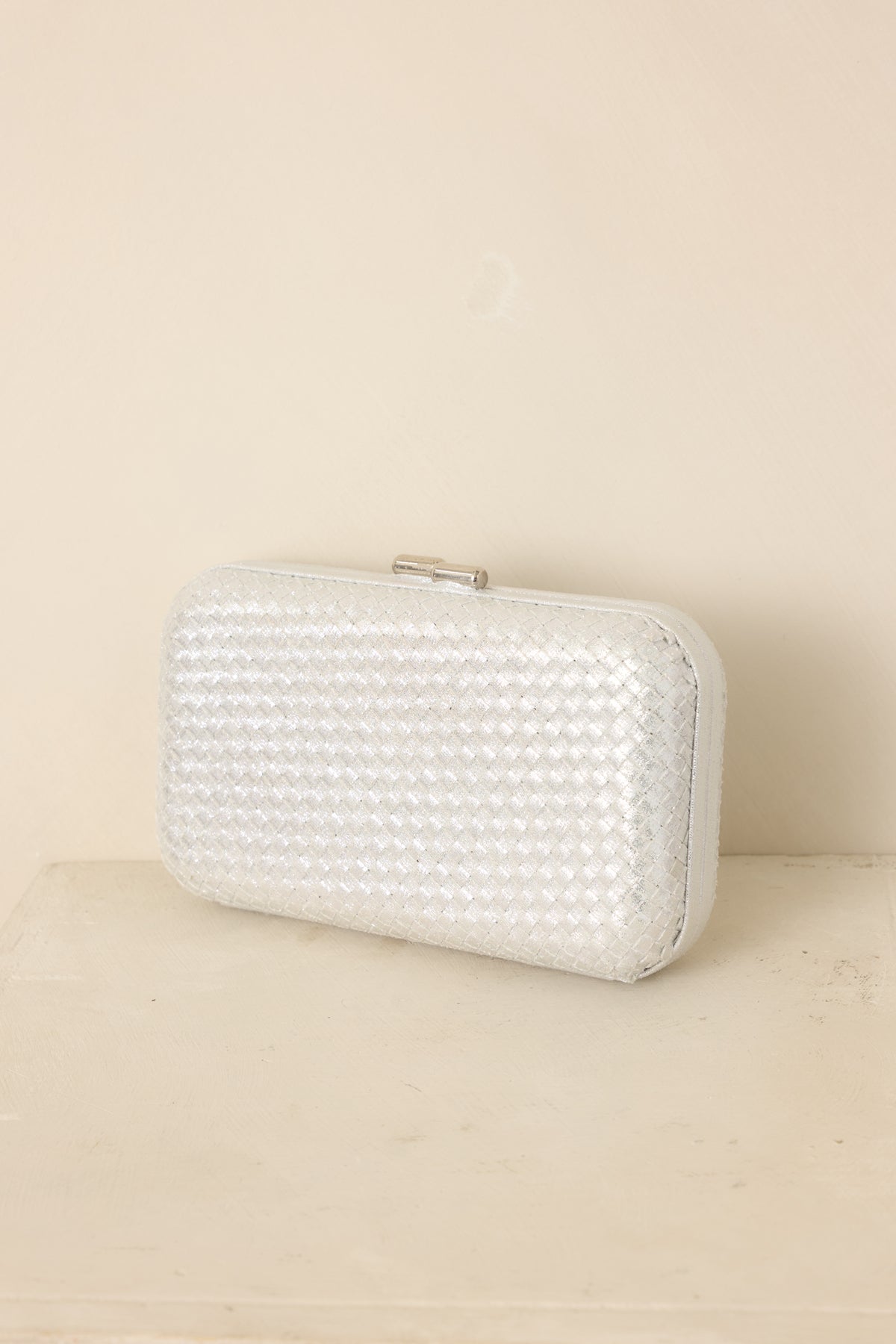 Silver woven clutch featuring a structured rectangular shape, hard case body, rounded edges, and optional chain strap.